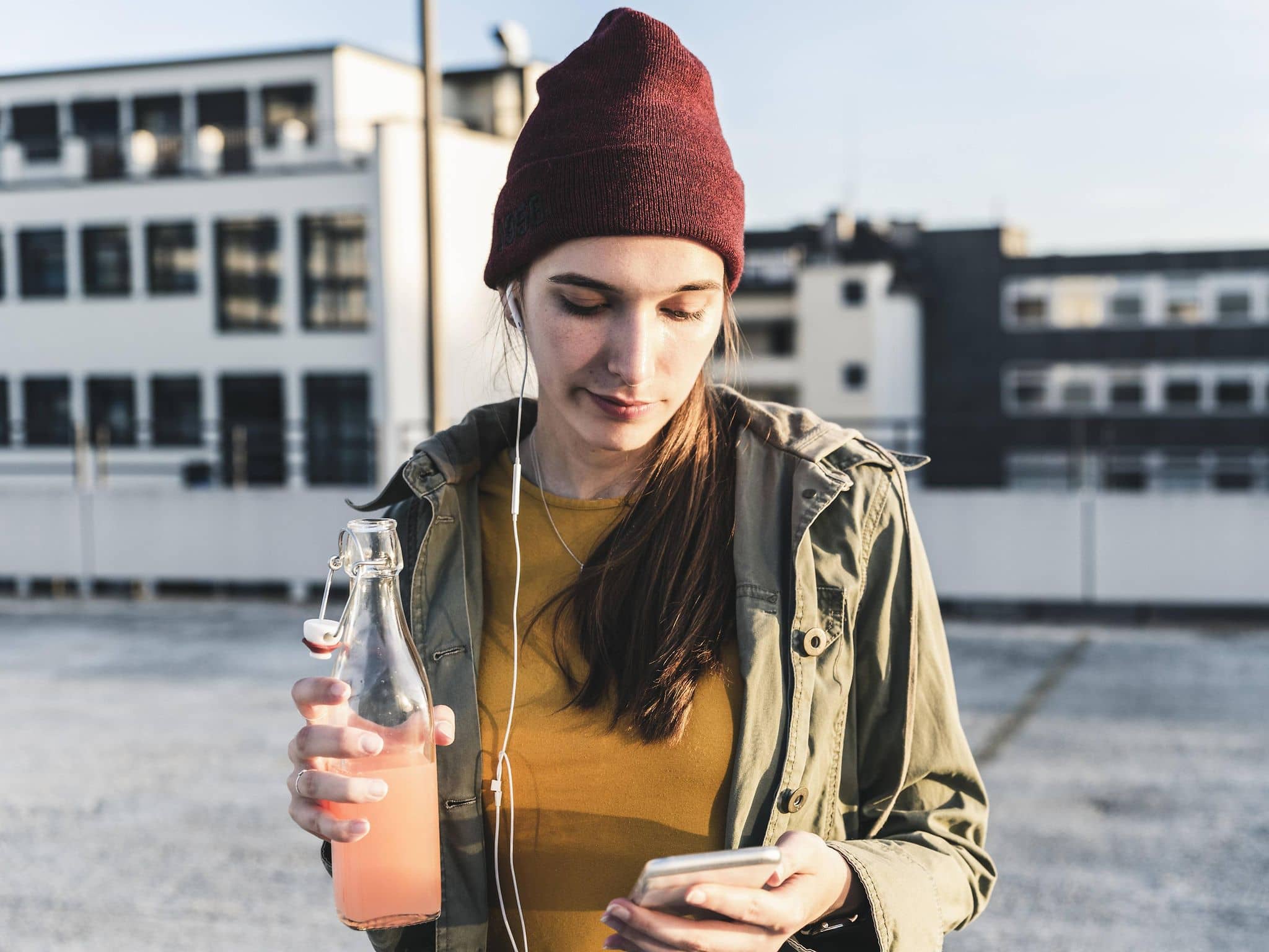 Junge Frau mit Drink und Handy in der Hand auf einem Parkdeck.