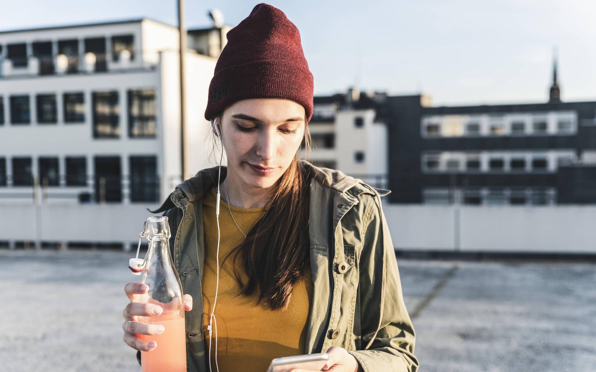 Junge Frau mit Drink und Handy in der Hand auf einem Parkdeck.
