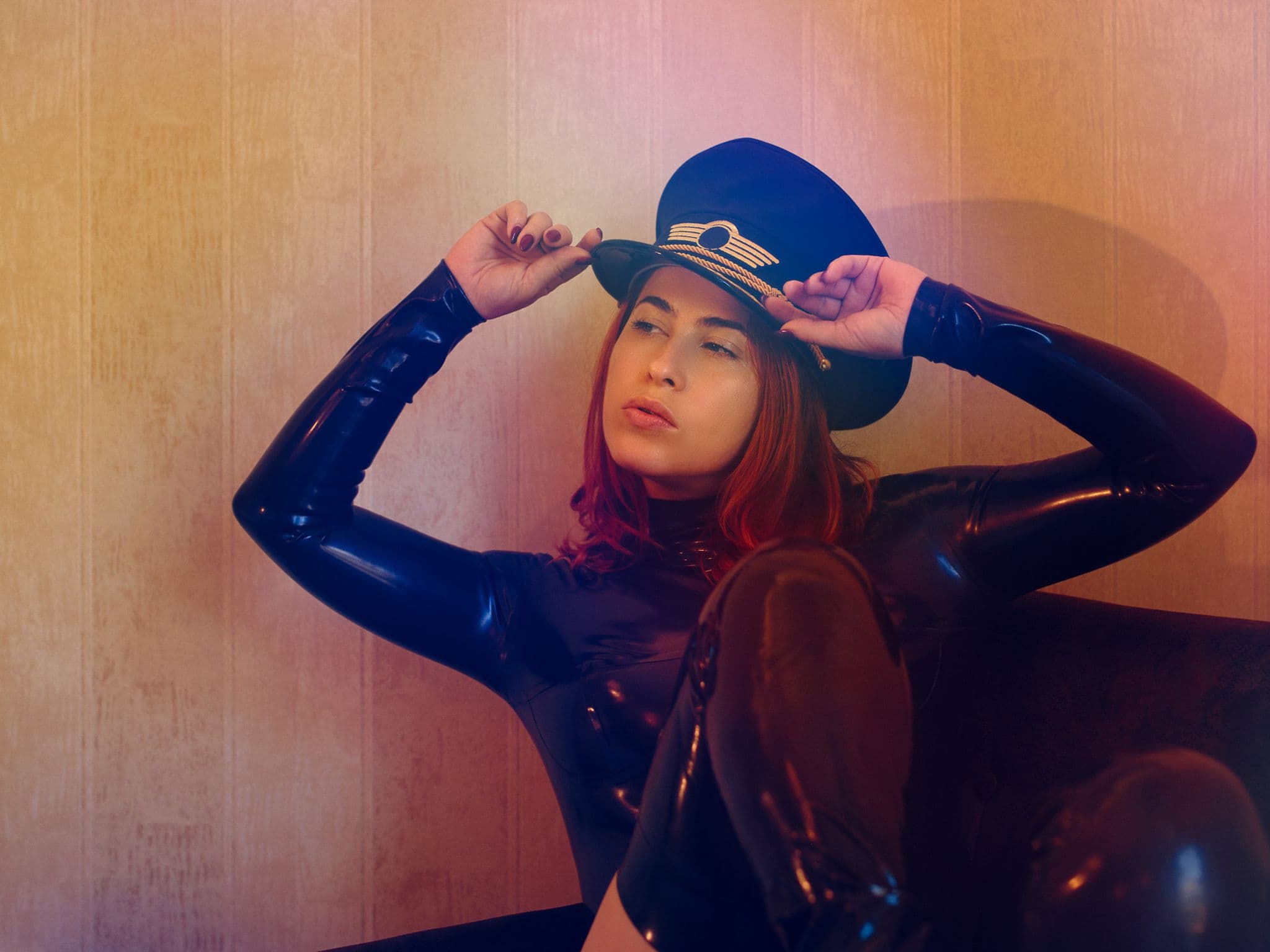 Fetisch: Eine Frau in Latexanzug und mit Uniformmütze sitzt auf einem Sofa