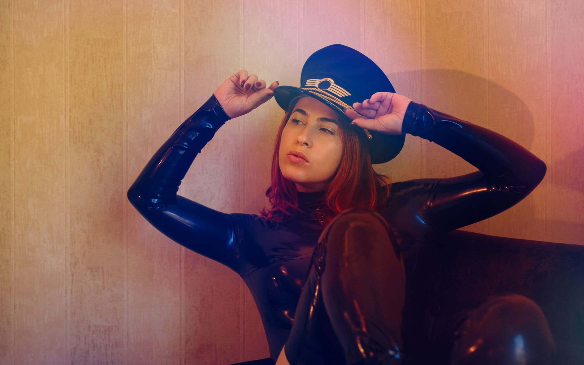 Fetisch: Eine Frau in Latexanzug und mit Uniformmütze sitzt auf einem Sofa