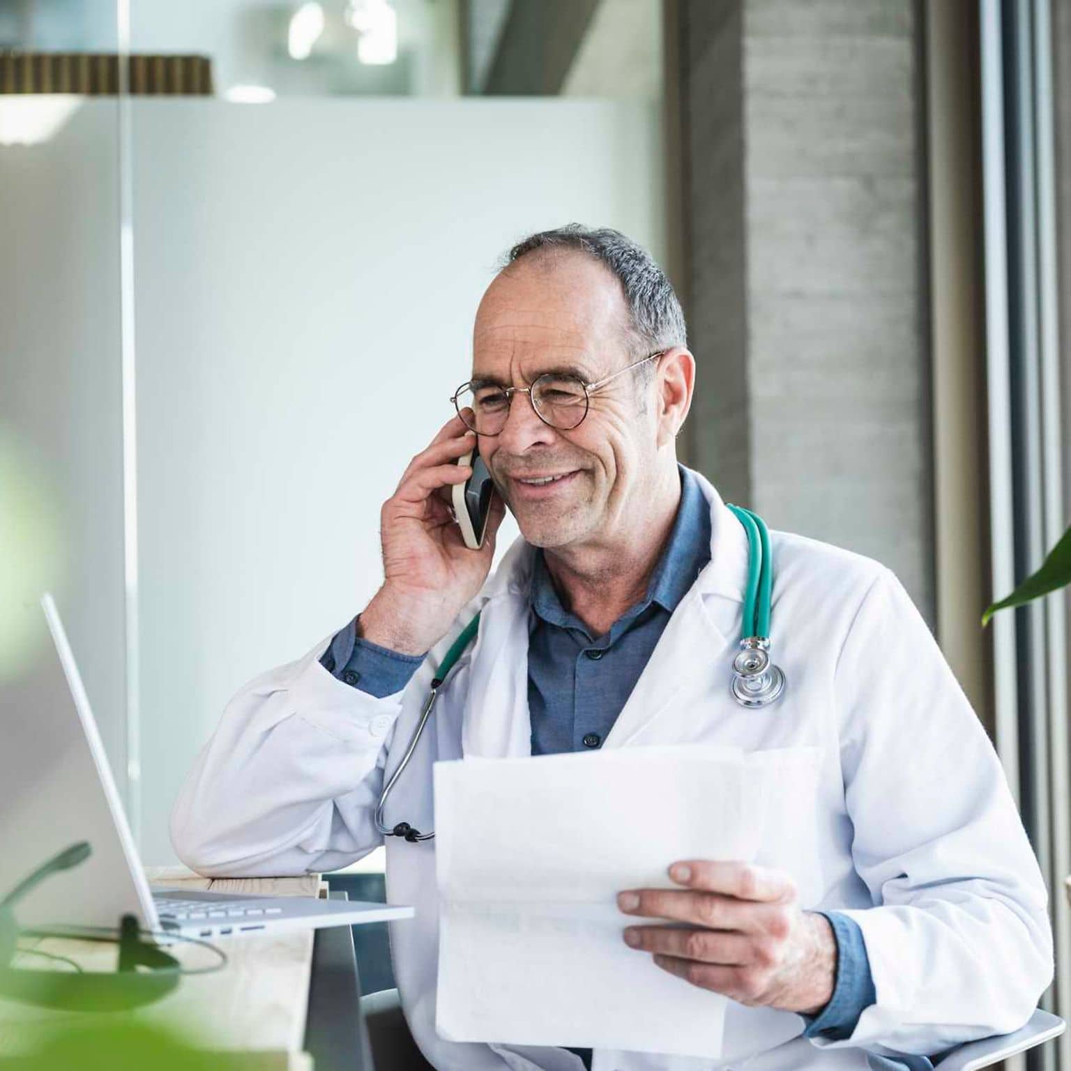Bild: Lächelnder Arzt telefoniert mit einem Bericht in der Hand.