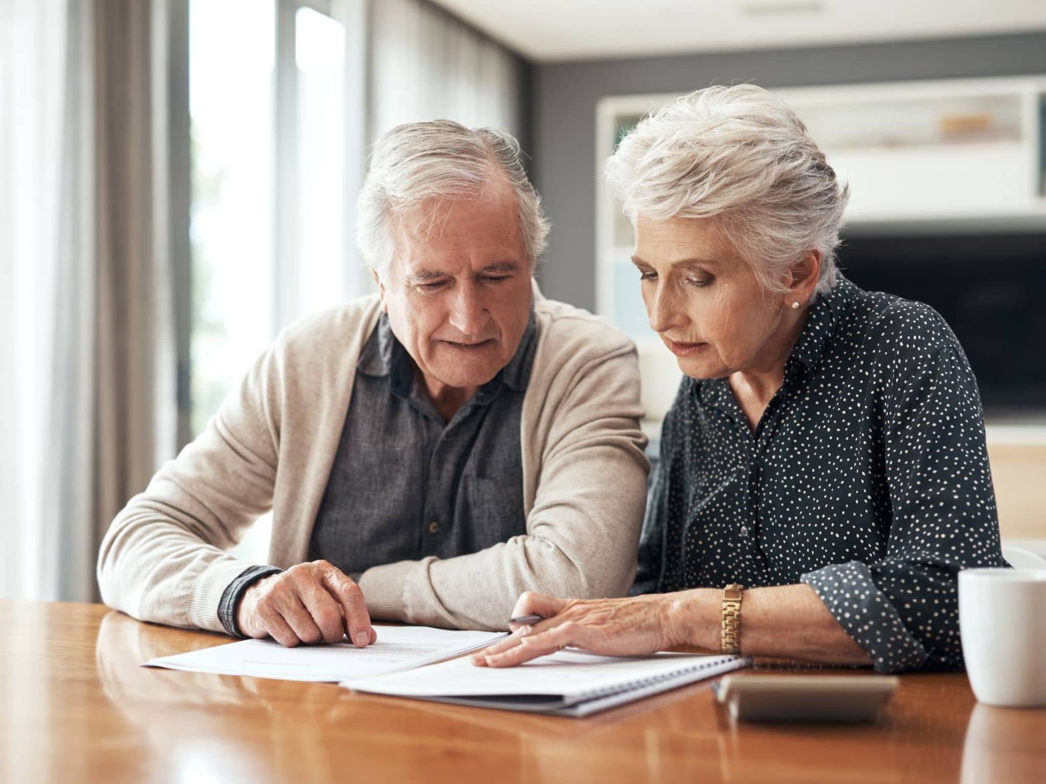 Seniorenpaar sitzt am Tisch und schaut gemeinsam auf Dokumente.