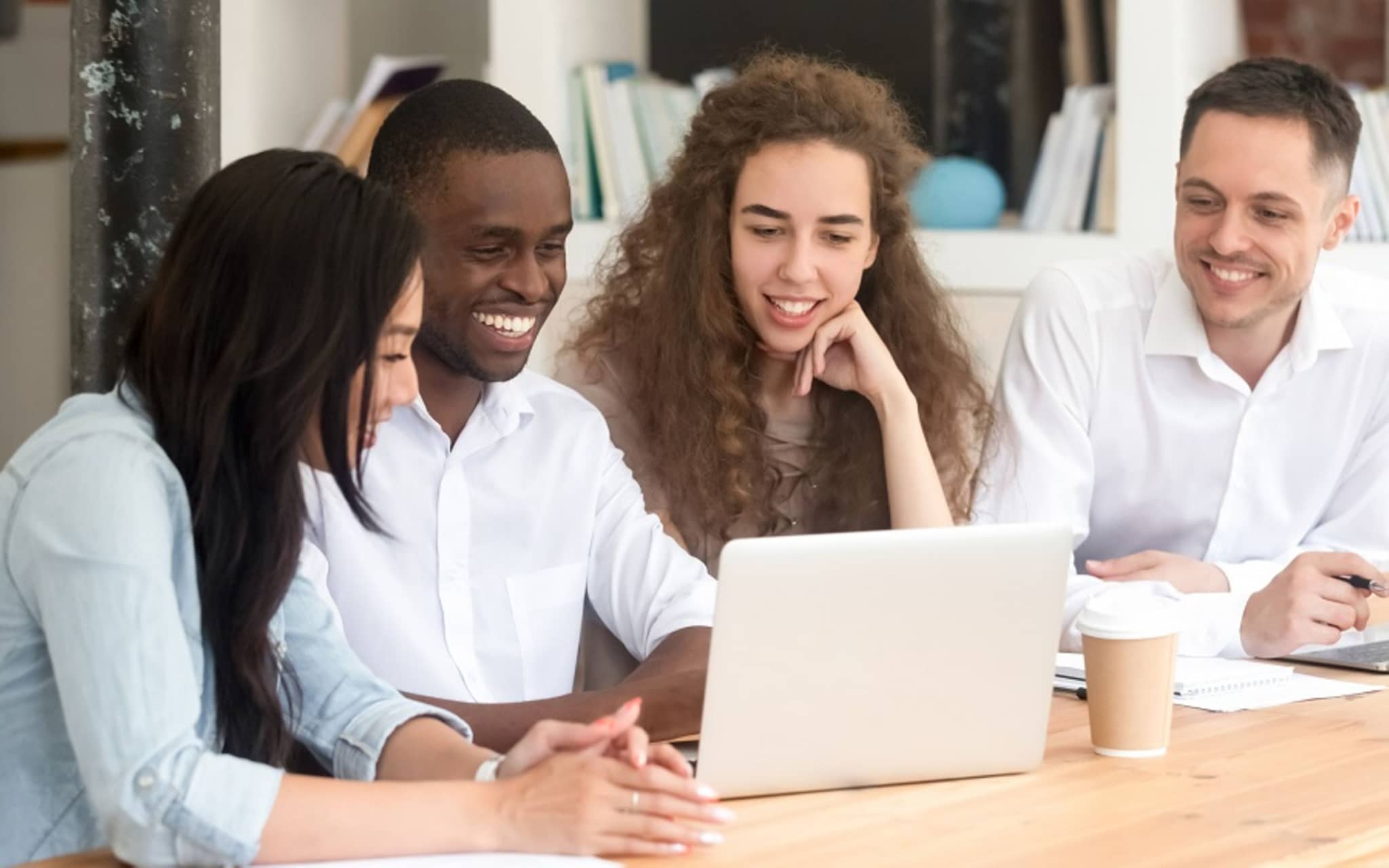 Mehrere junge Personen sitzen vor einem LAptop und lachen.