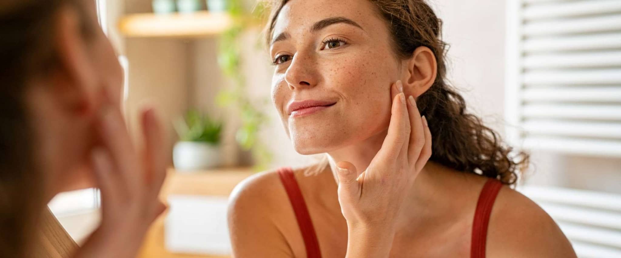 Hautkrebs-Screening: Junge Frau steht vor dem Spiegel und betrachtet Ihre Haut.