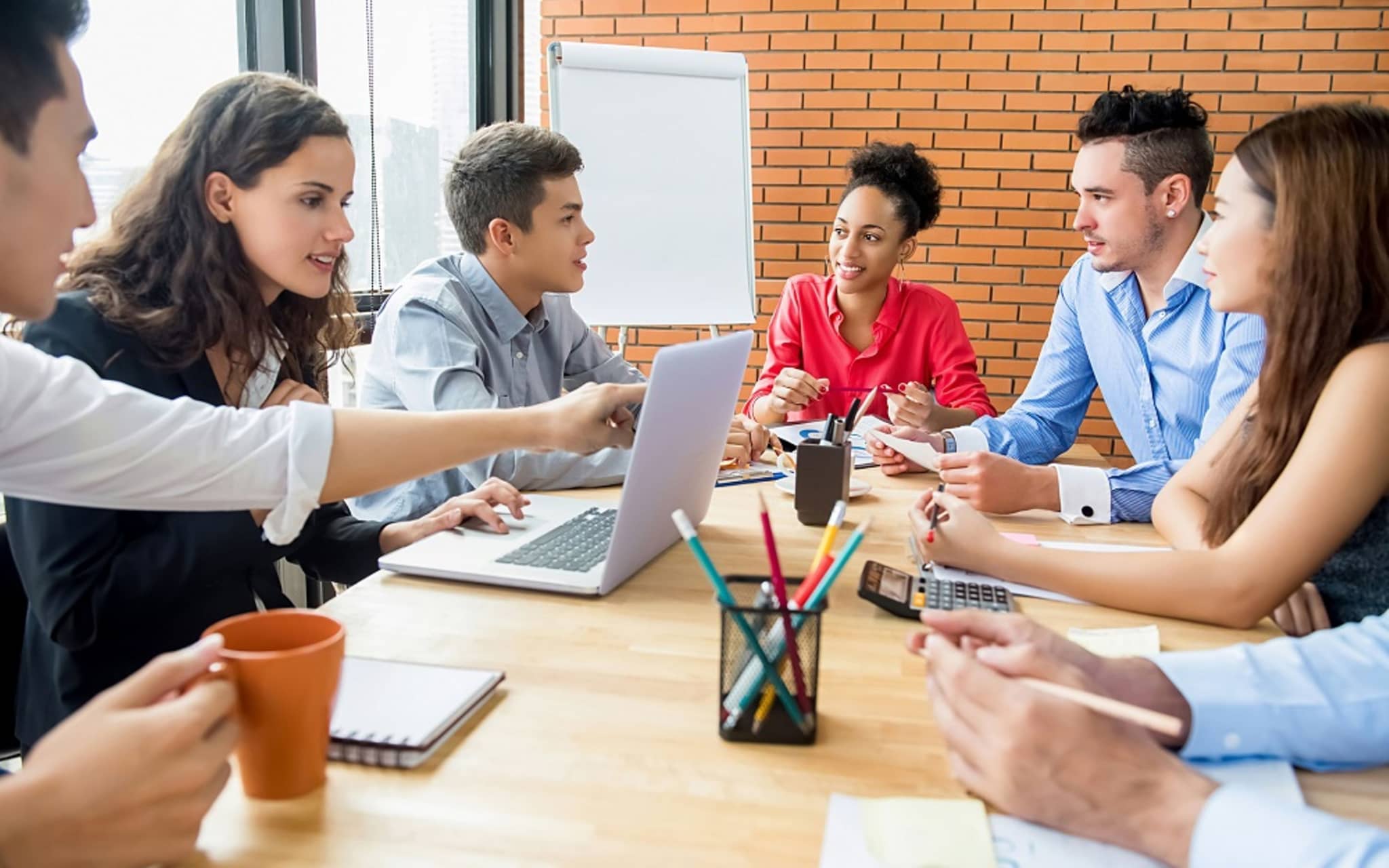 Junge Menschen sitzen am Tisch mit Laptop und diskutieren.