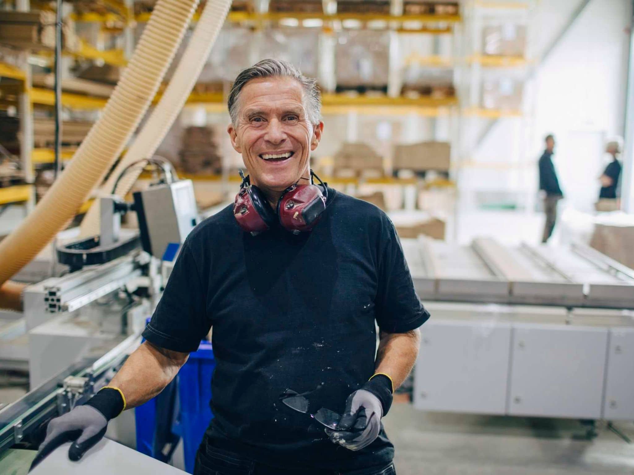 Bild: Älterer Herr steht in einem Sägewerk und lächelt in die Kamera.