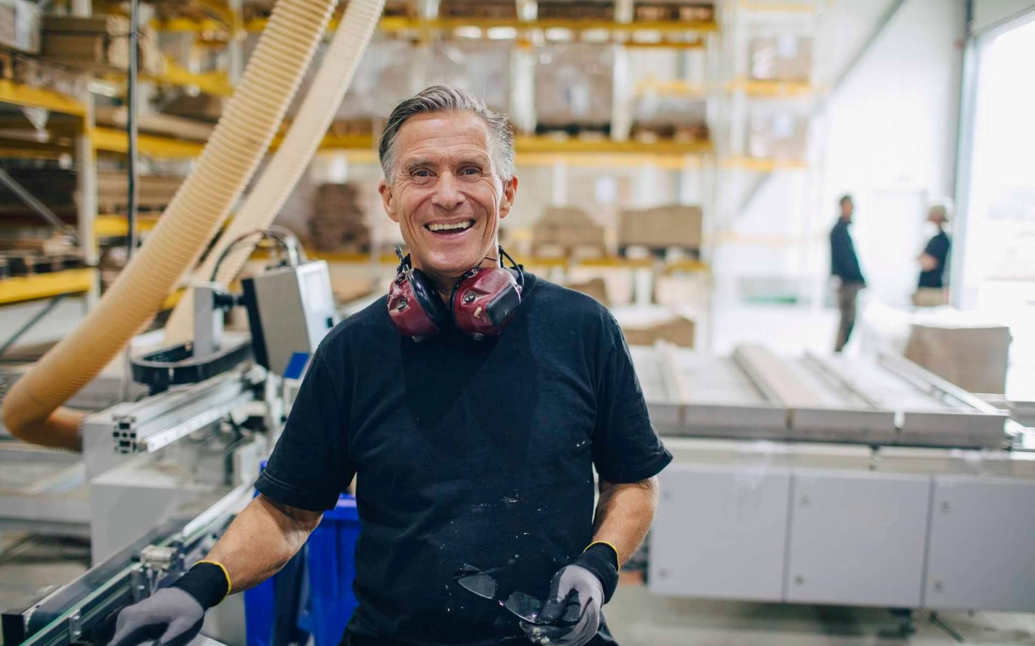 Bild: Älterer Herr steht in einem Sägewerk und lächelt in die Kamera.