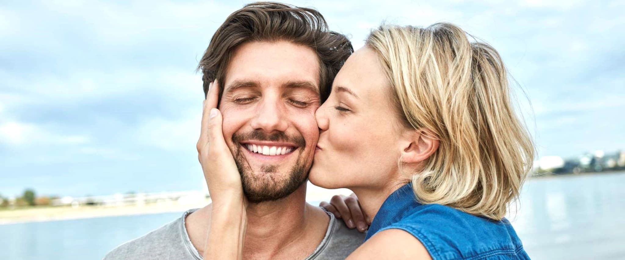 Professionelle Zahnreinigung: Junge Frau küsst Ihren Partner auf die Wange.