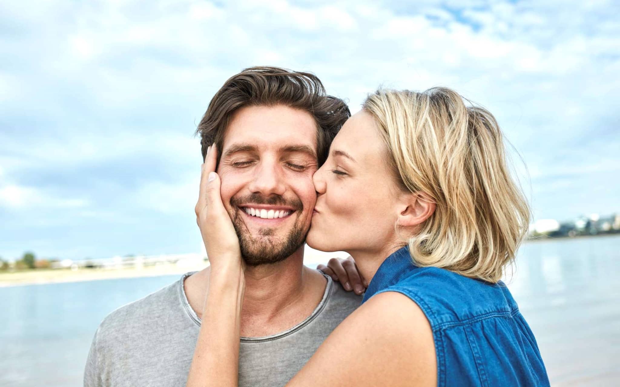 Professionelle Zahnreinigung: Junge Frau küsst Ihren Partner auf die Wange.