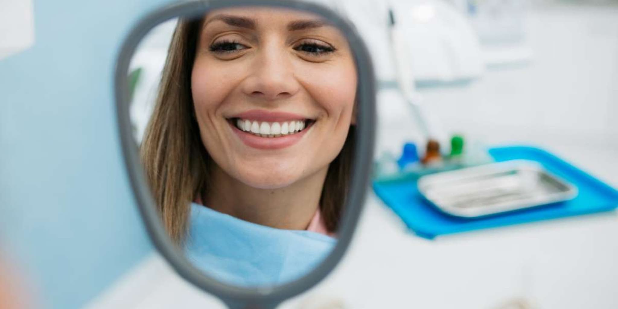 Professionelle Zahnreinigung: Junge Frau schaut sich nach der Behandlung ihre Zähne im Spiegel an.