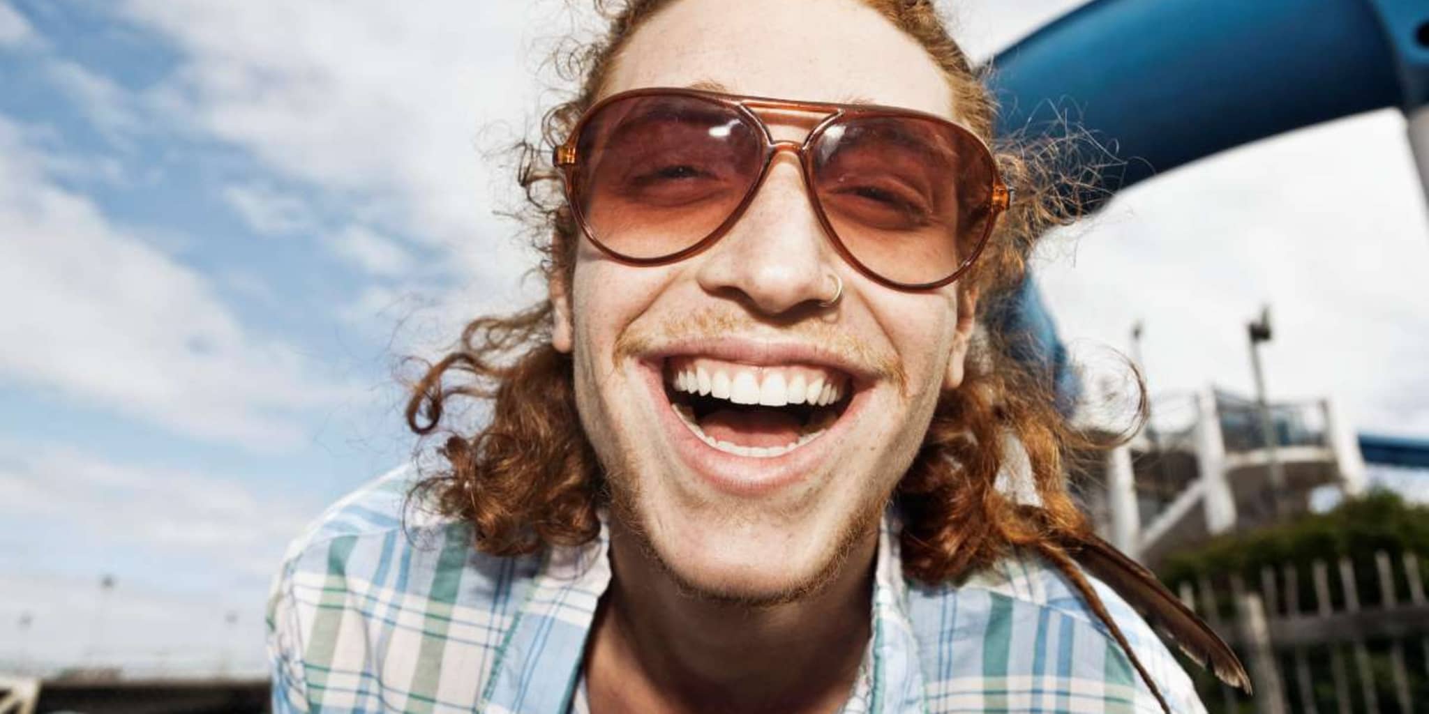 Professionelle Zahnreinigung: Junger Mann mit Sonnenbrille strahlt in die Kamera.