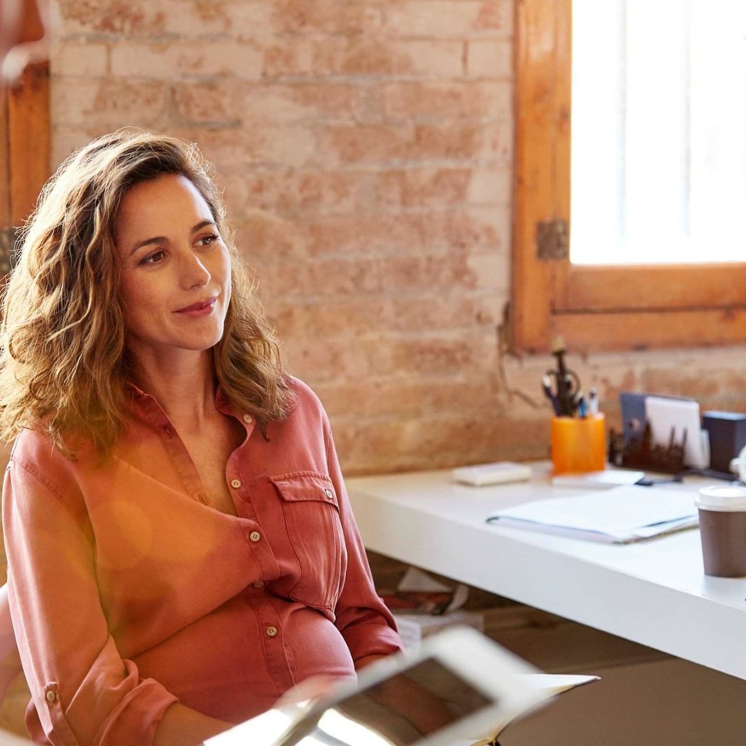 Krankenversicherung für Arbeitnehmerinnen: Schwangere Frau sitzt am Schreibtisch im Büro