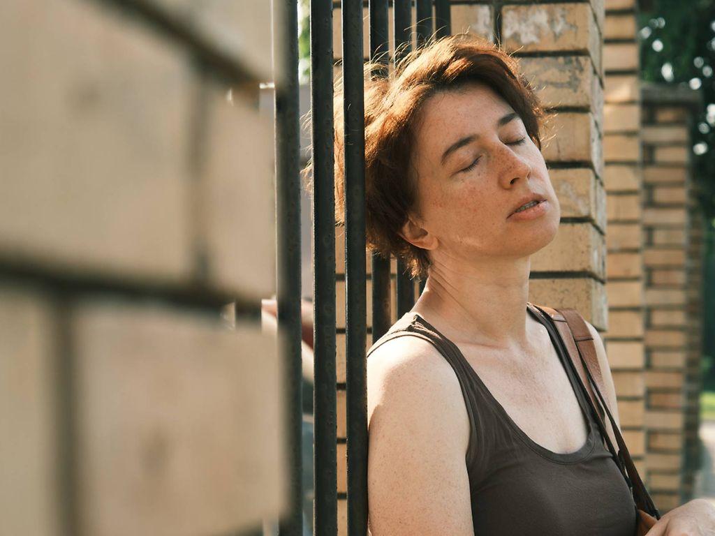 Hitzeerschöpfung: Frau lehnt erschöpft am Zaun