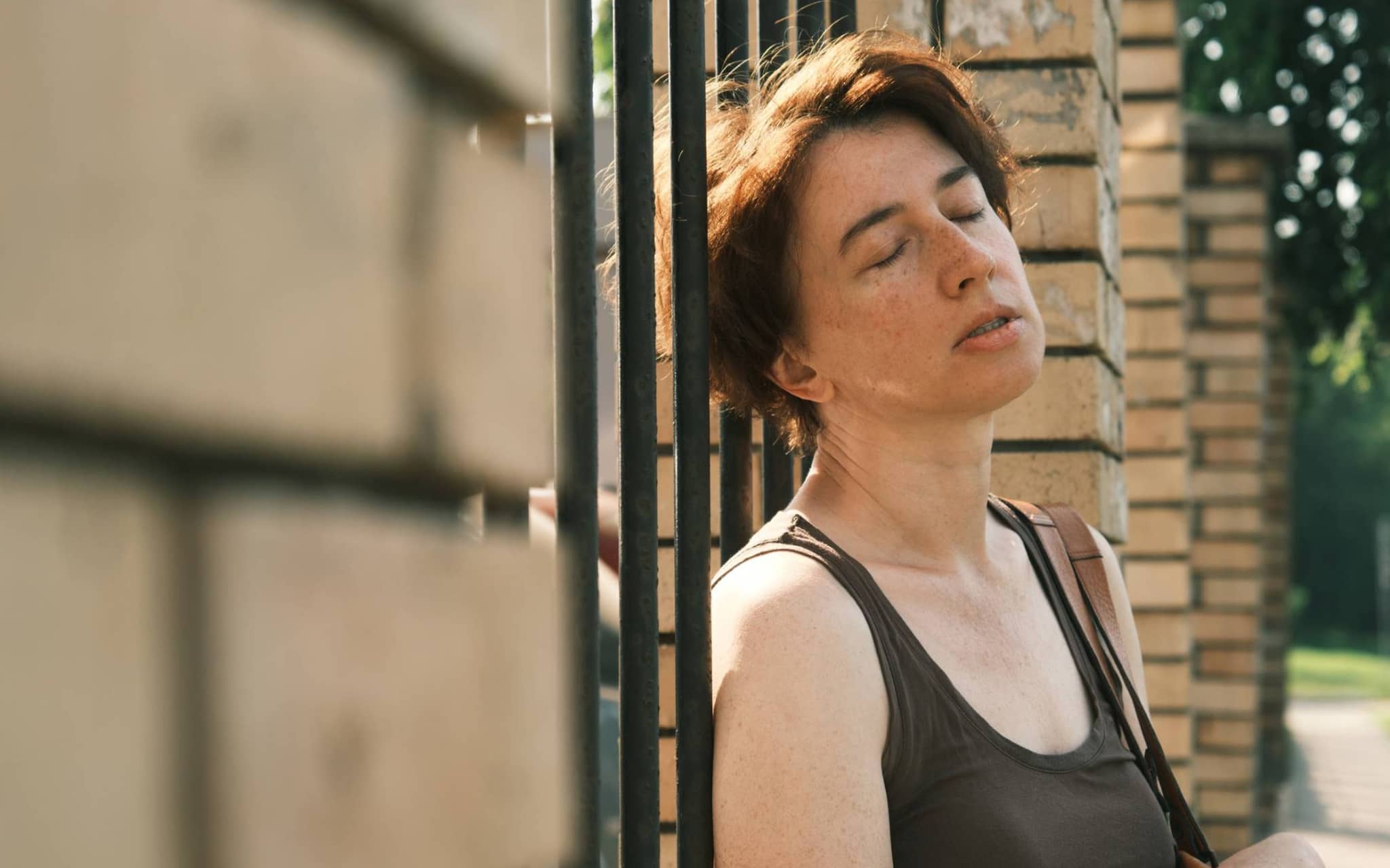Hitzeerschöpfung: Frau lehnt erschöpft am Zaun