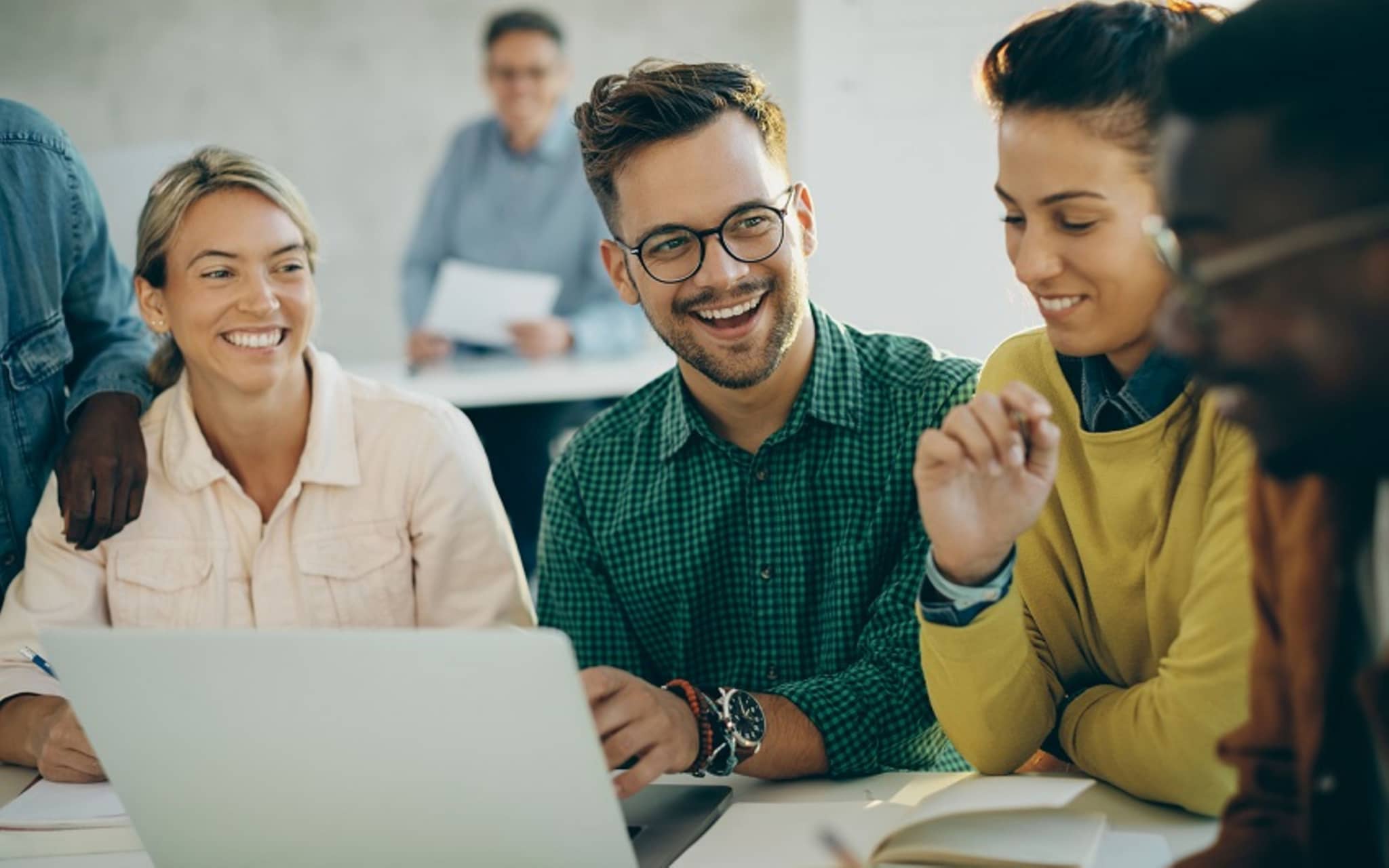 Gruppe sitzt am Tisch vor Laptop und lacht.