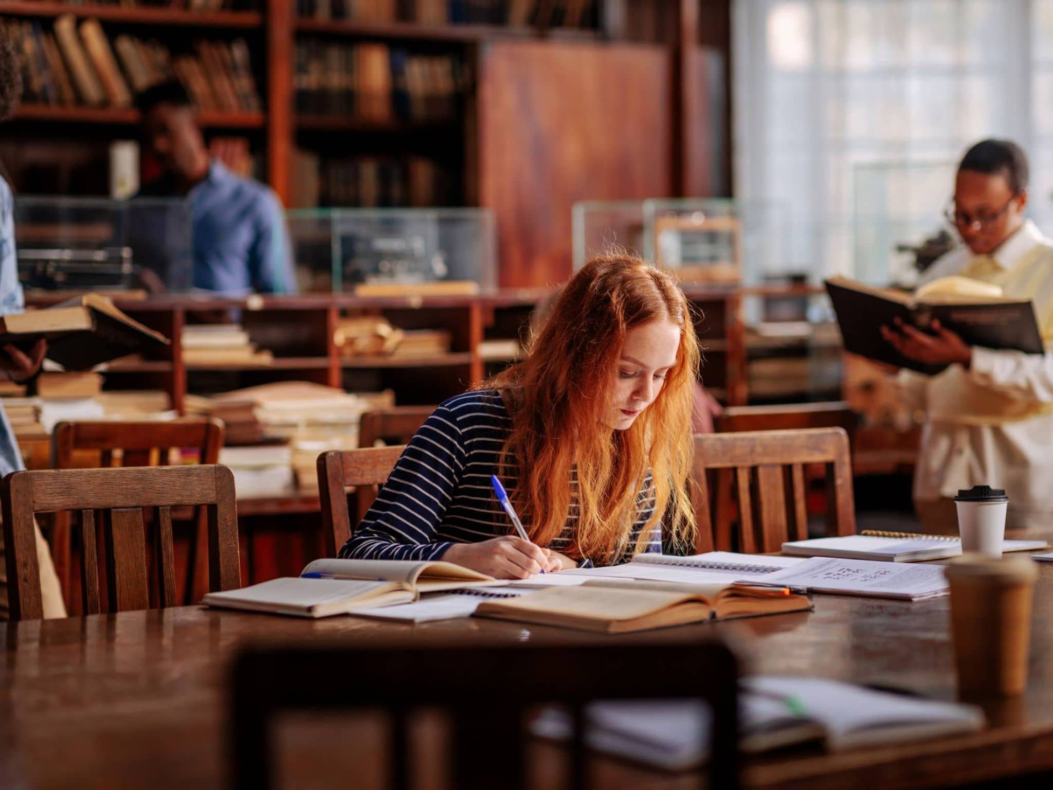 Krankenversicherung für Studierende aus dem Ausland: Junge Frau liest ein Buch in einer Bibliothek.