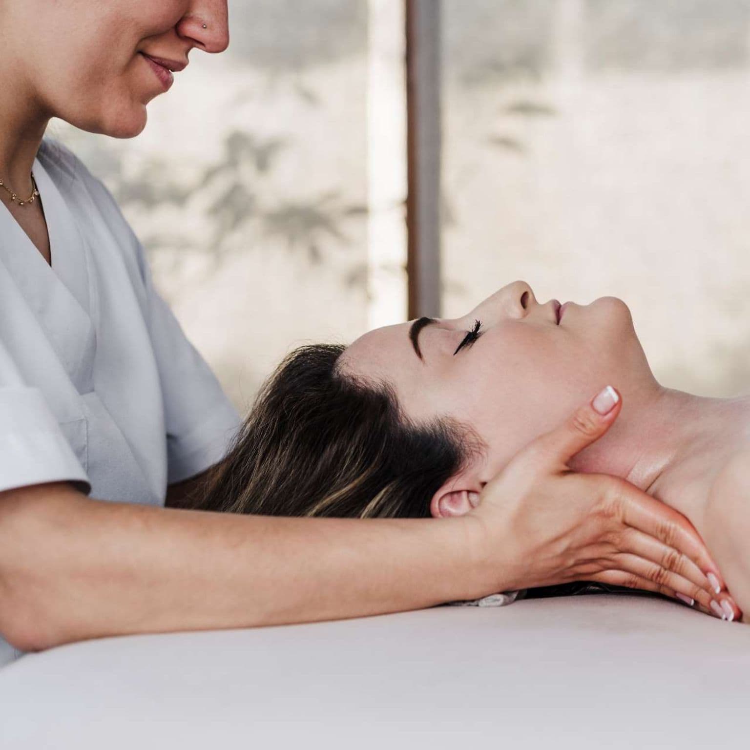 Osteopathie: Junge Frau liegt auf dem Rücken und wird am Nacken behandelt.