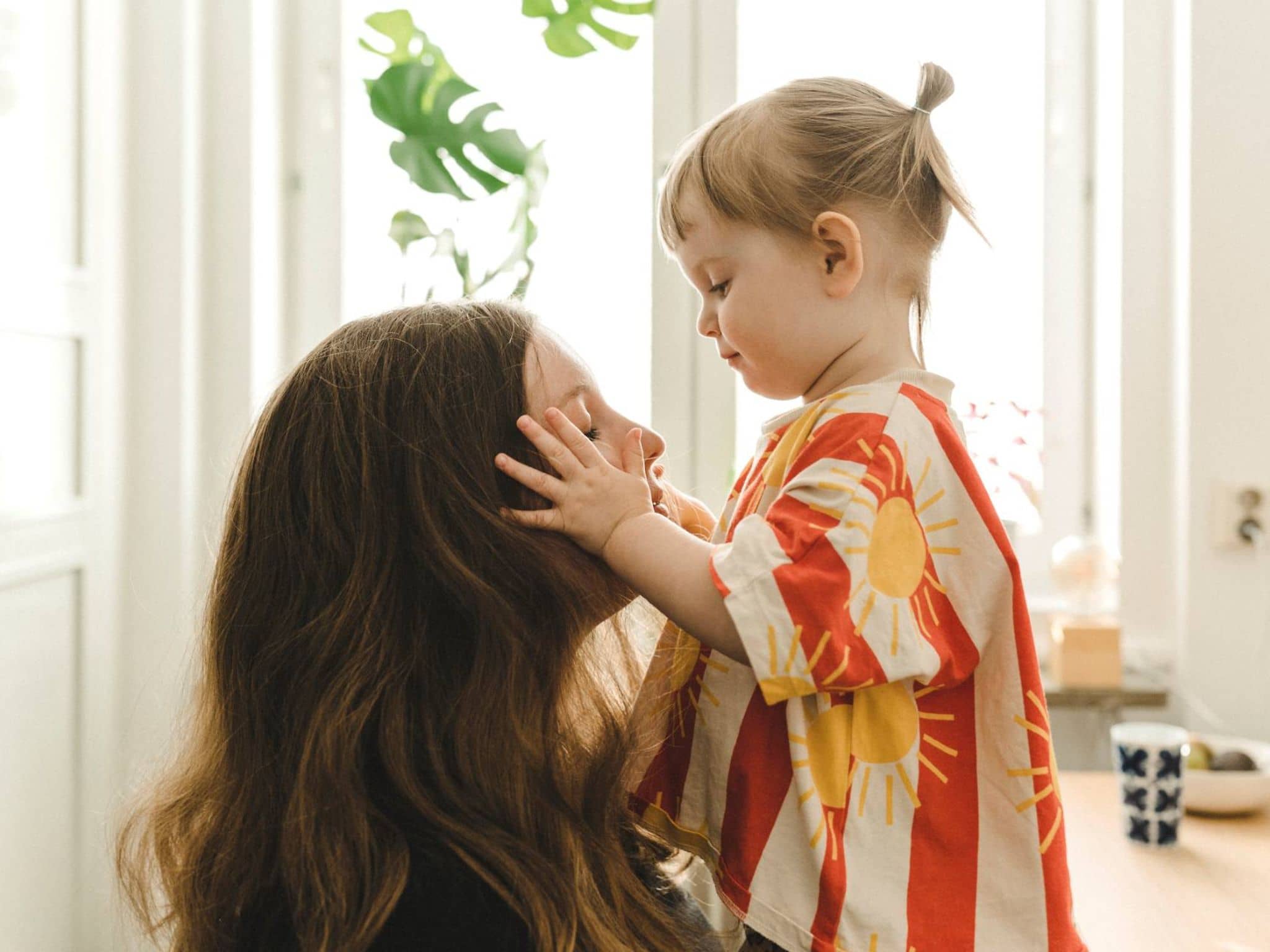 Krankenversicherung während der Elternzeit: Kleines Mädchen legt liebevoll die Hände auf das Gesicht ihrer Mutter