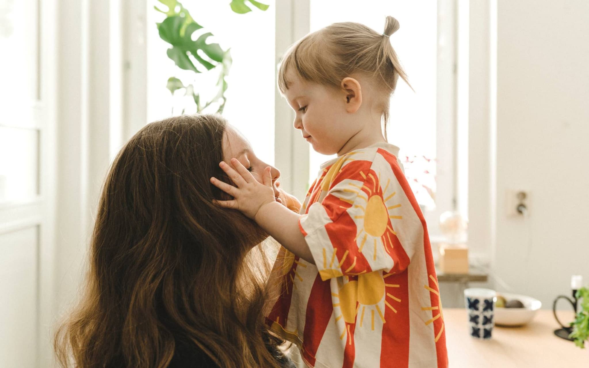 Krankenversicherung während der Elternzeit: Kleines Mädchen legt liebevoll die Hände auf das Gesicht ihrer Mutter