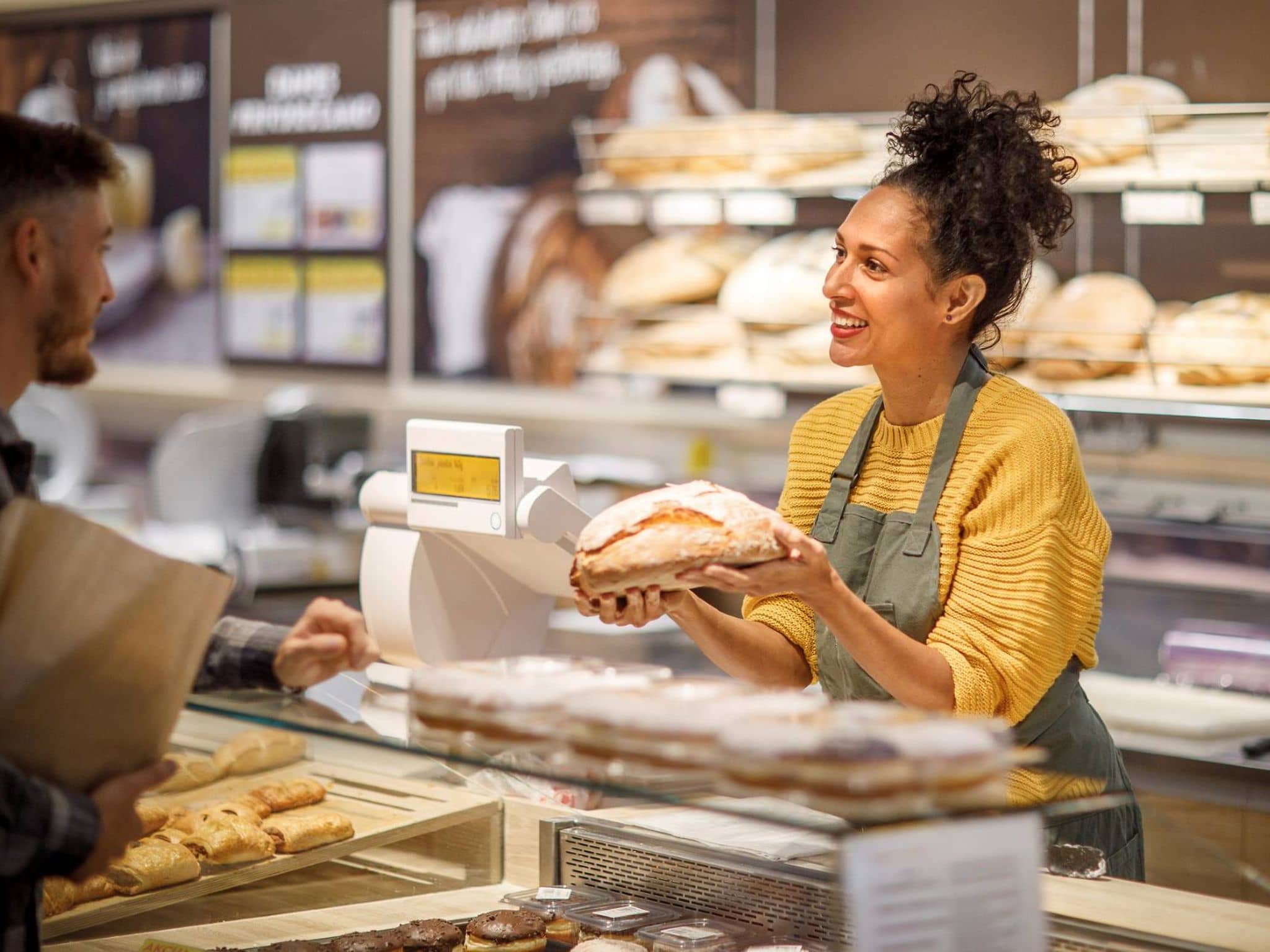 Krankenversicherung im Minijob: Freundliche Bäckereiverkäuferin präsentiert einem Kunden Brotlaib