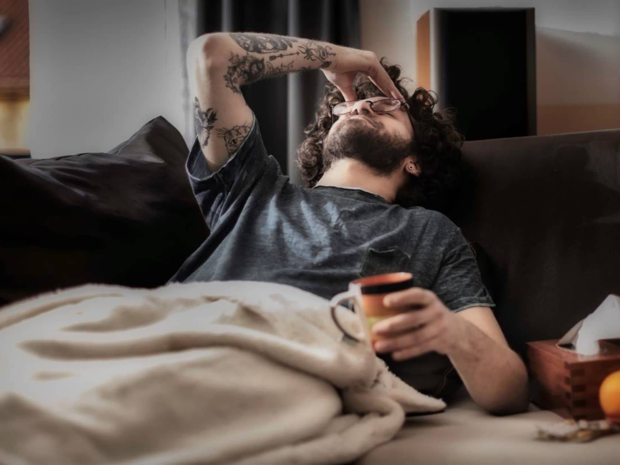 Krankengeld für Selbstständige: Mann liegt krank auf der Couch und hält sich den Kopf