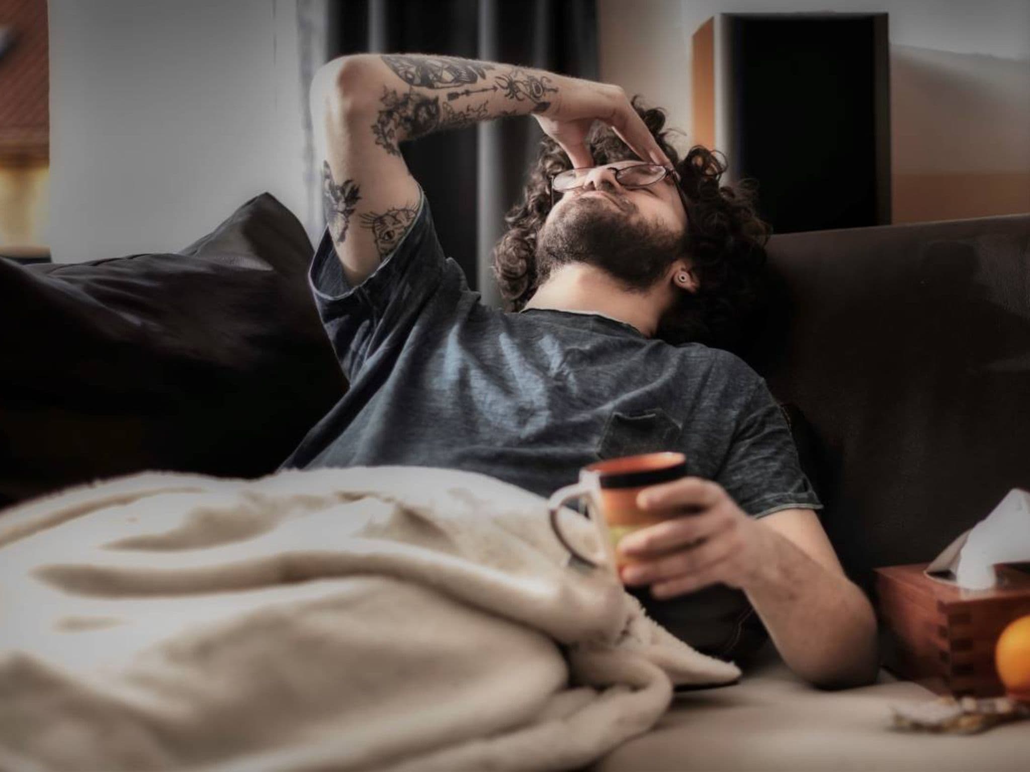 Krankengeld für Selbstständige: Mann liegt krank auf der Couch und hält sich den Kopf
