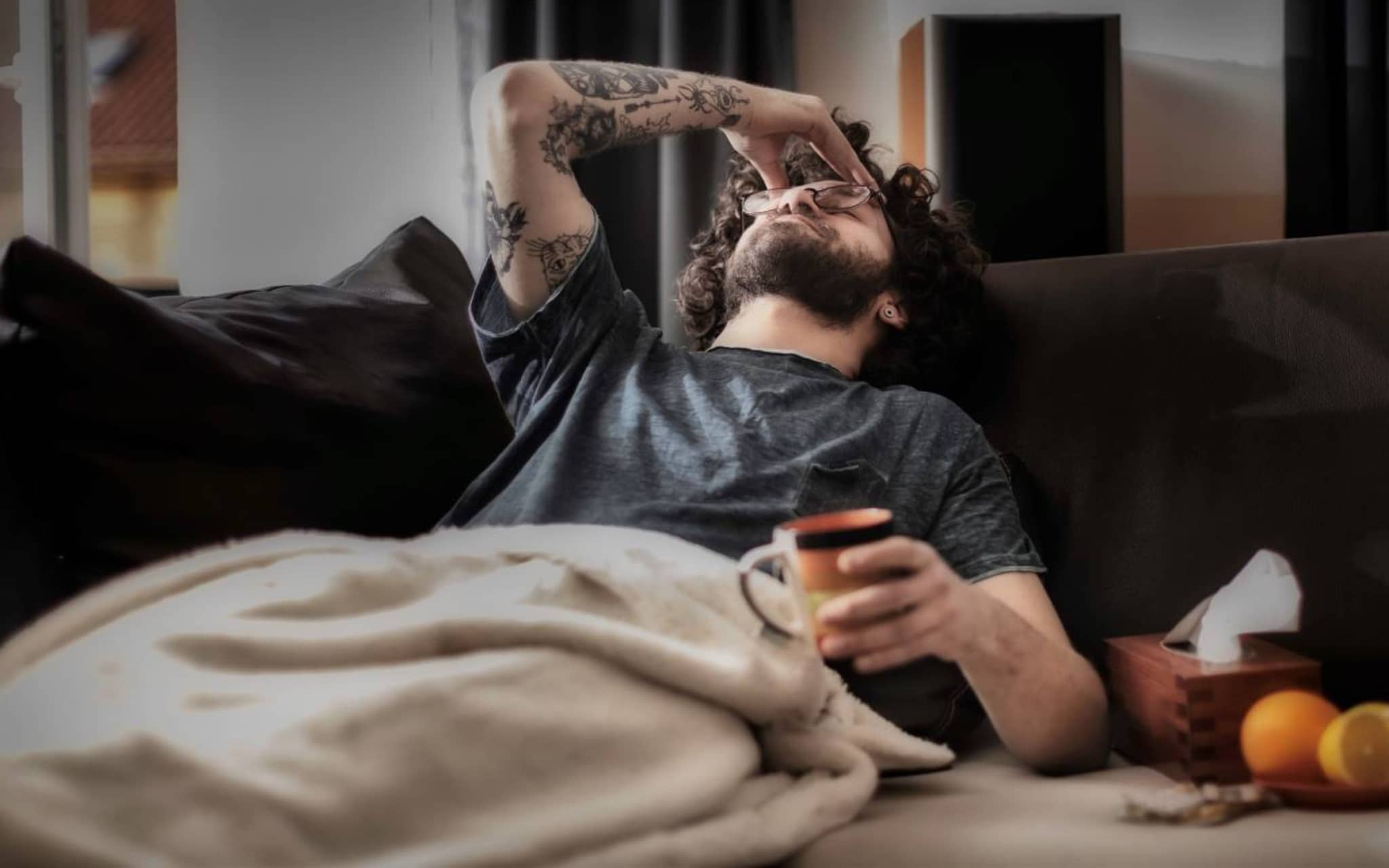 Krankengeld für Selbstständige: Mann liegt krank auf der Couch und hält sich den Kopf