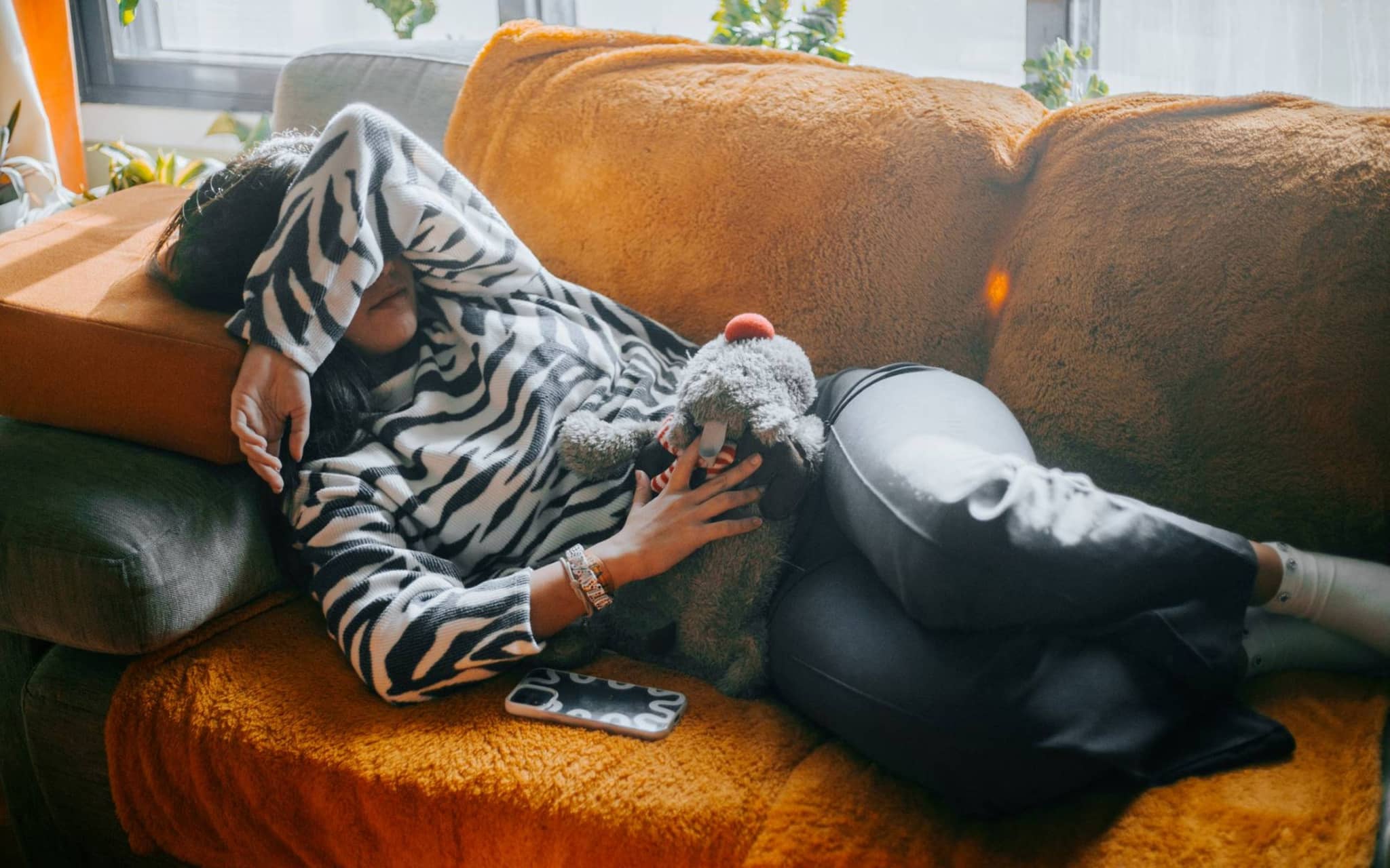 Symbolbild Menstruationsschmerzen: Junge Frau liegt mit Menstruationsschmerzen auf dem Sofa.