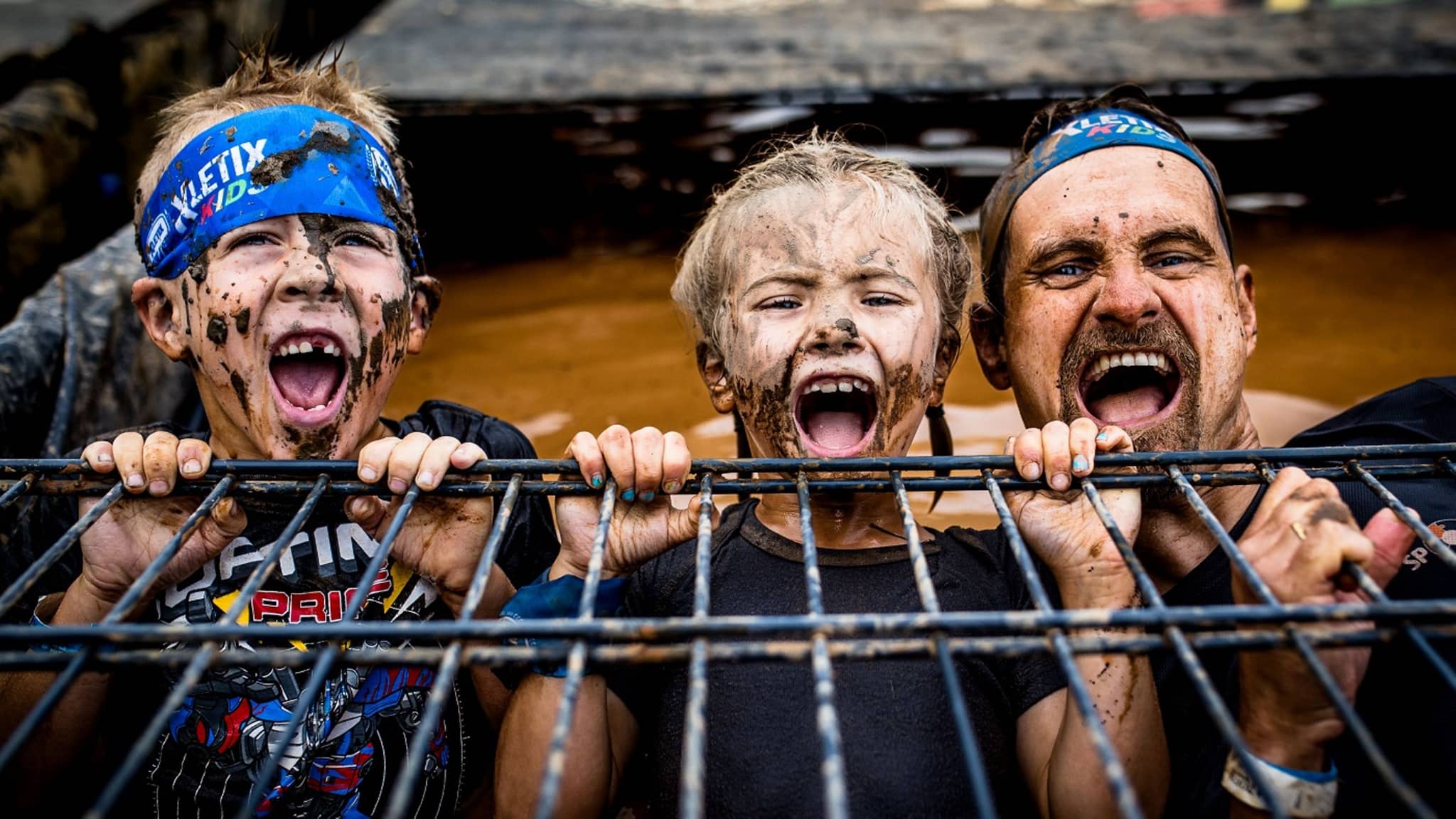 Vater mit zwei Kindern bei der Xletics-Veranstaltung - alle drei sind schlammverschmiert.