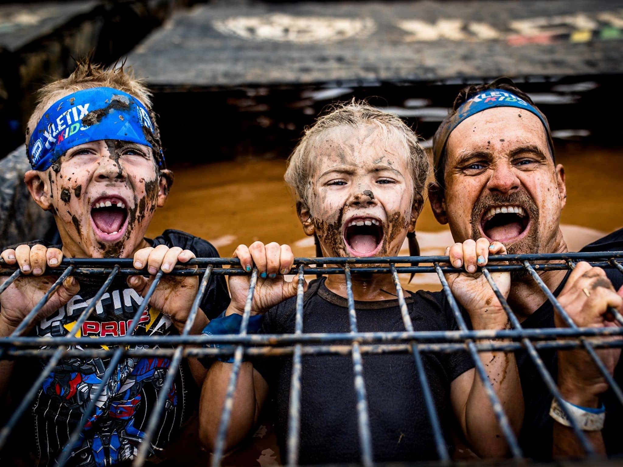Vater mit zwei Kindern bei der Xletics-Veranstaltung - alle drei sind schlammverschmiert.