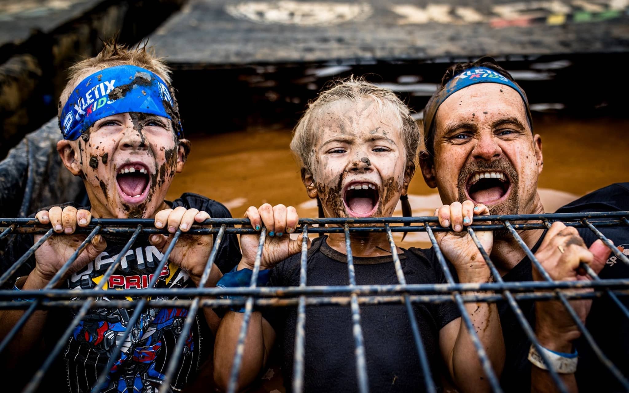 Vater mit zwei Kindern bei der Xletics-Veranstaltung - alle drei sind schlammverschmiert.