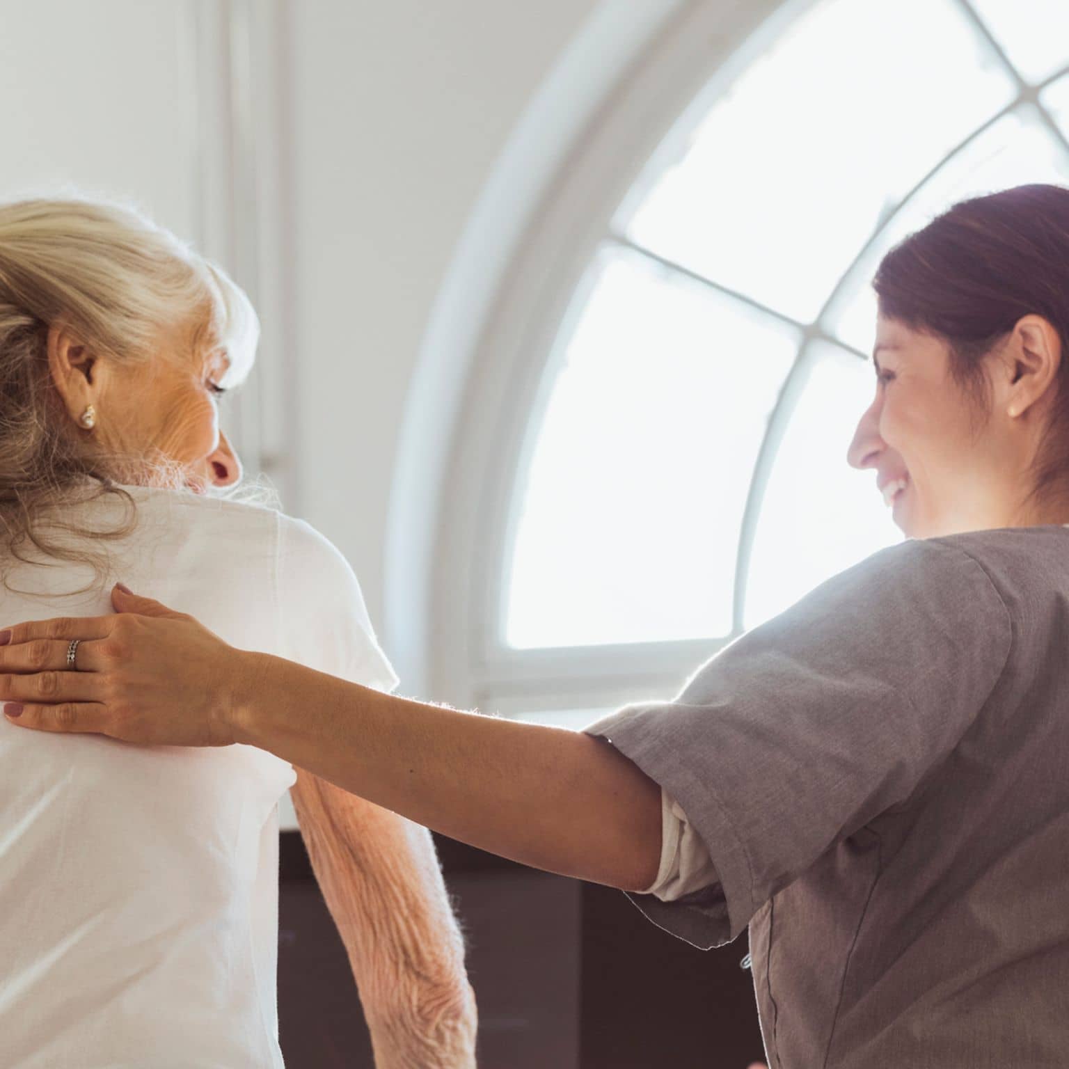 Bild: Pflegekraft lächelt eine ältere Dame an.