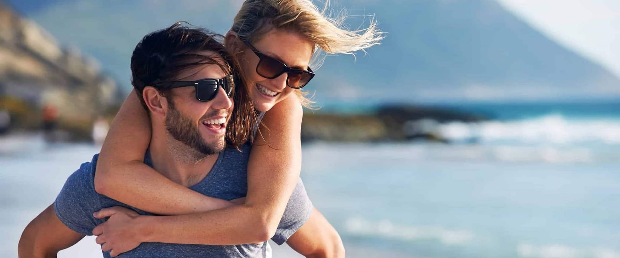 Garantietarif 120: Mann trägt Frau huckepack am Strand entlang.