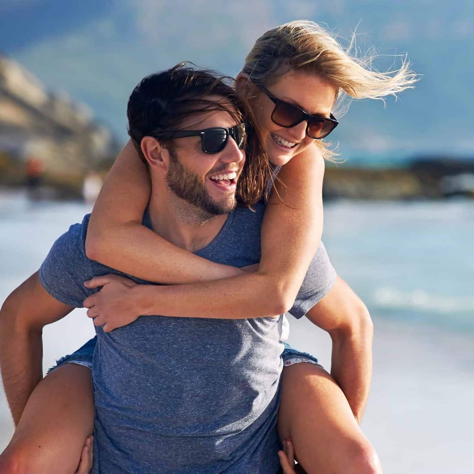 Garantietarif 120: Mann trägt Frau huckepack am Strand entlang.