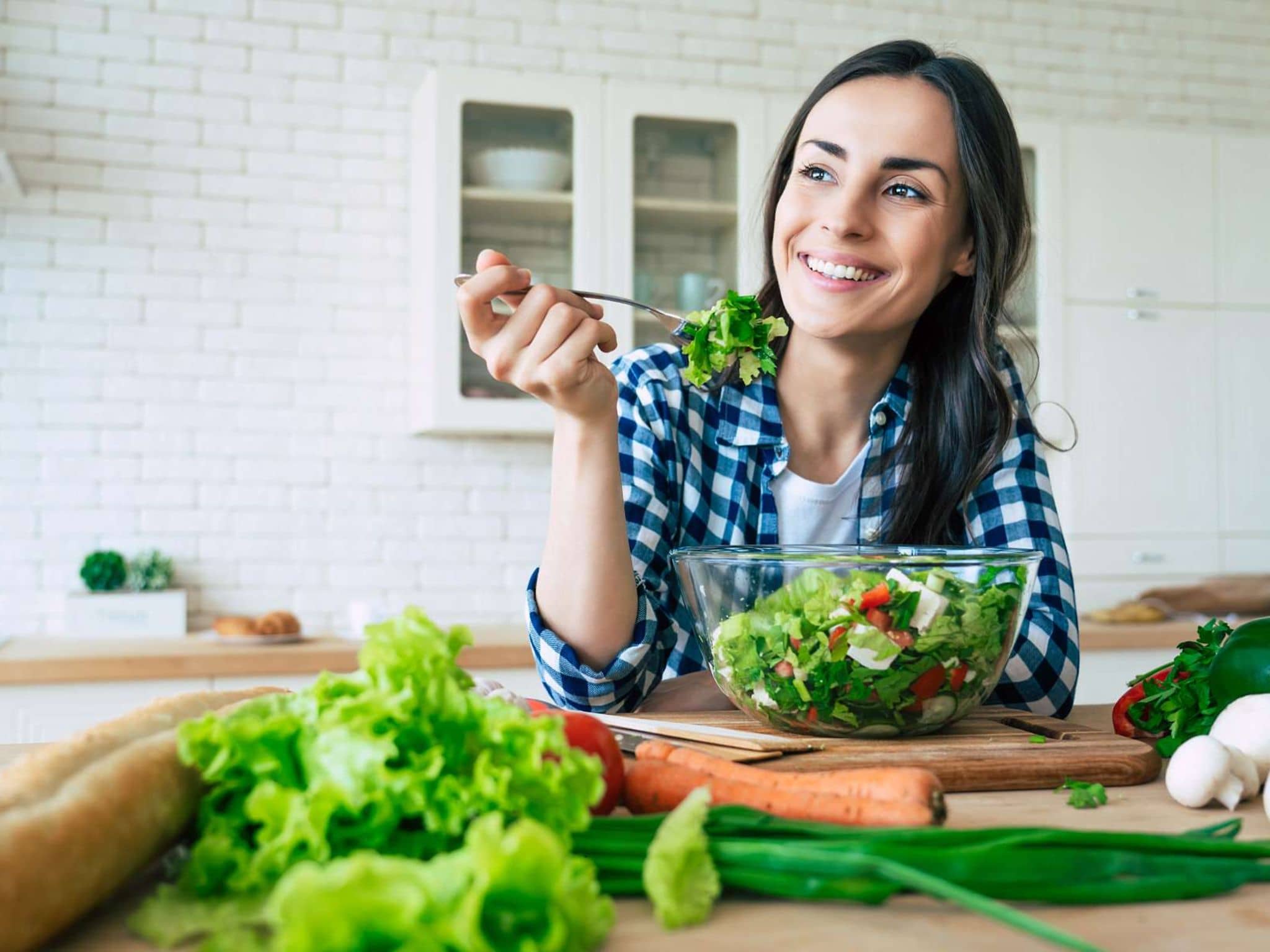 Fit & Cash: Junge Frau sitzt in ihrer Küche und isst einen Salat.