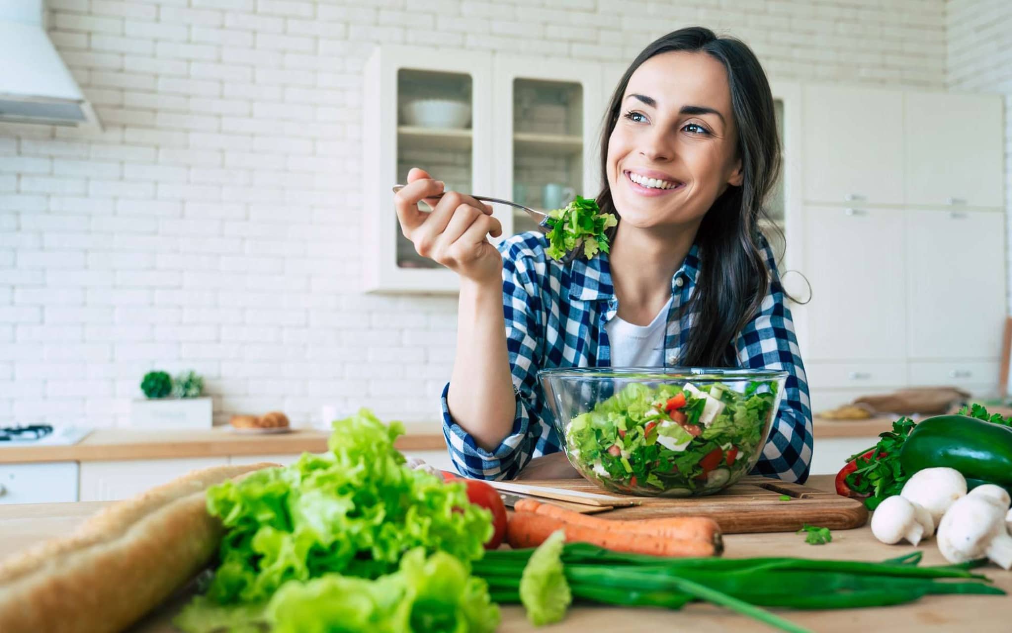 Fit & Cash: Junge Frau sitzt in ihrer Küche und isst einen Salat.