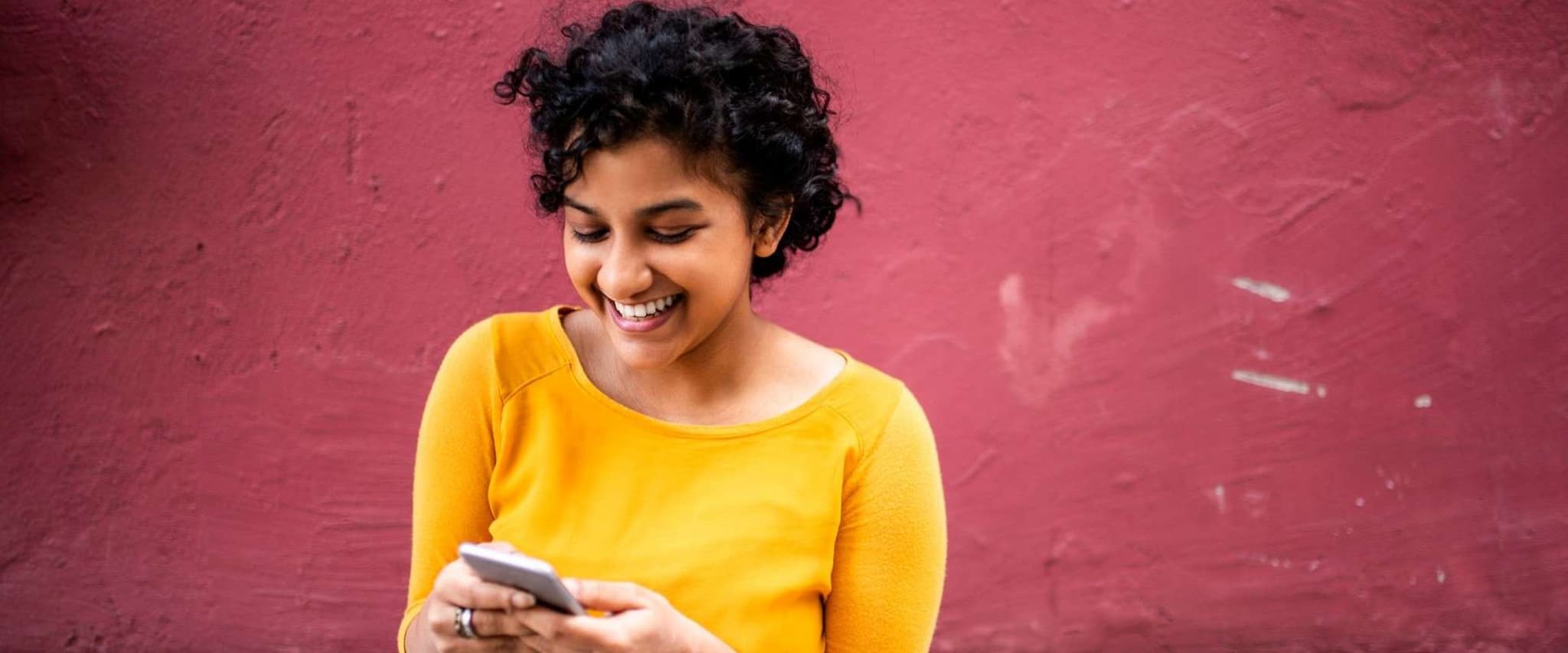 DAK Garantietraif 90 für Azubis: Junge Frau steht vor einer roten Wand und schaut auf ihr Handy.