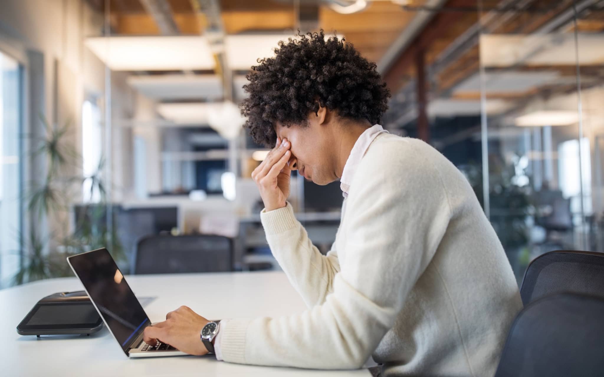 Person sitzt im Büro vor Laptop und hält sich nachdenklich die Stirn.