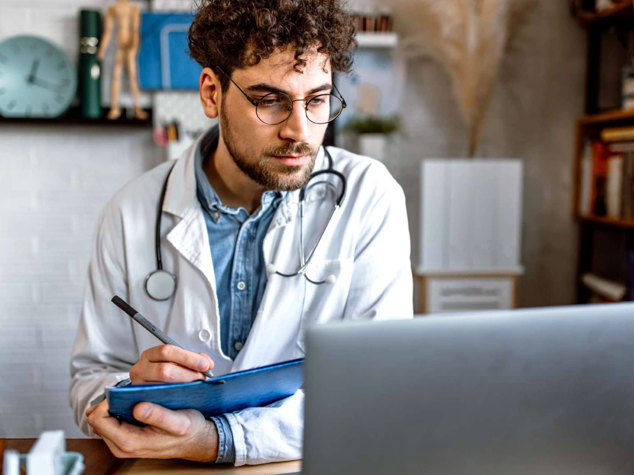 Bild: Arzt sitzt am Computer und notiert sich etwas.