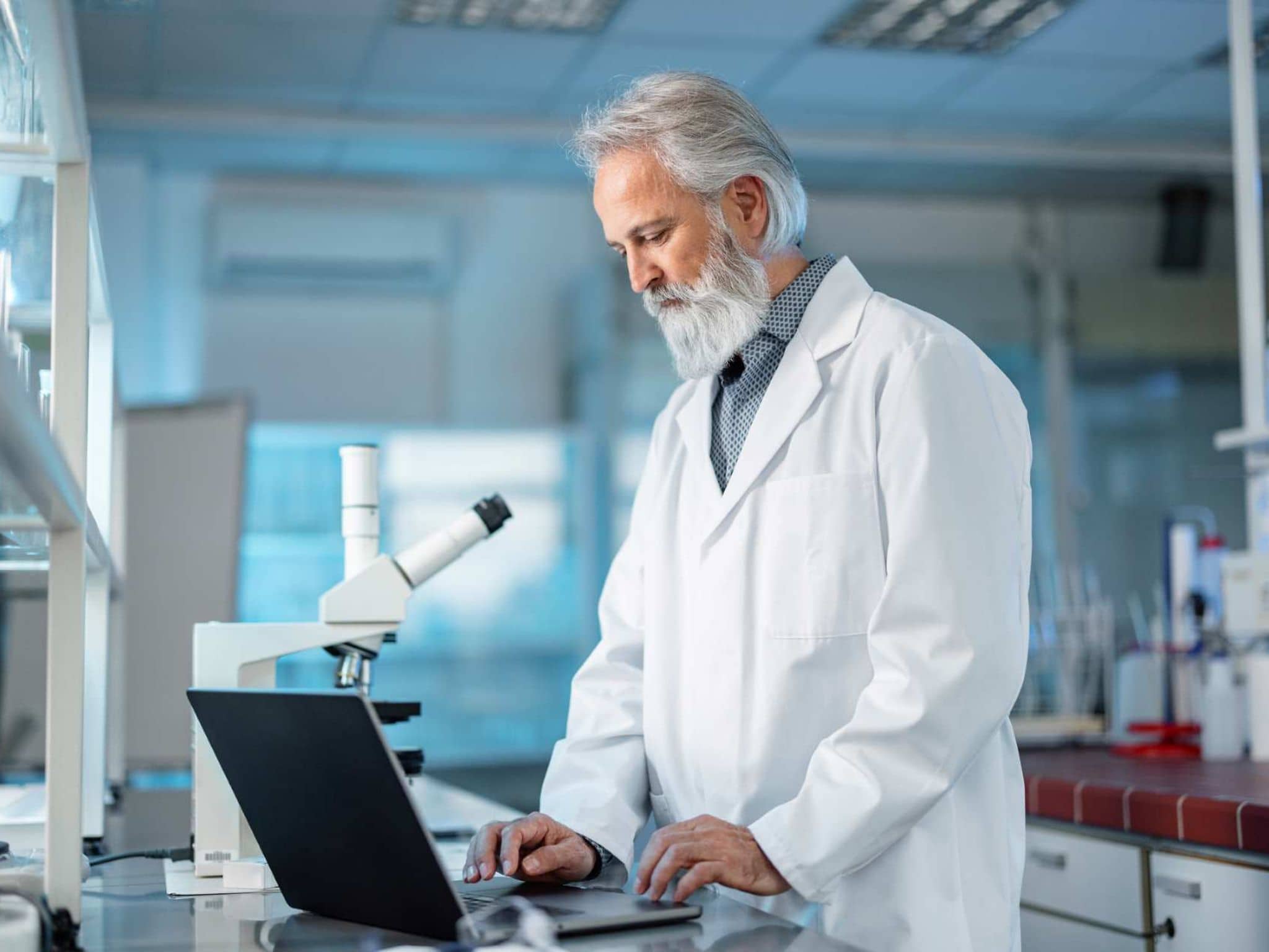 Bild: Chemiker steht im Labor und schaut etwas im Laptop nach.