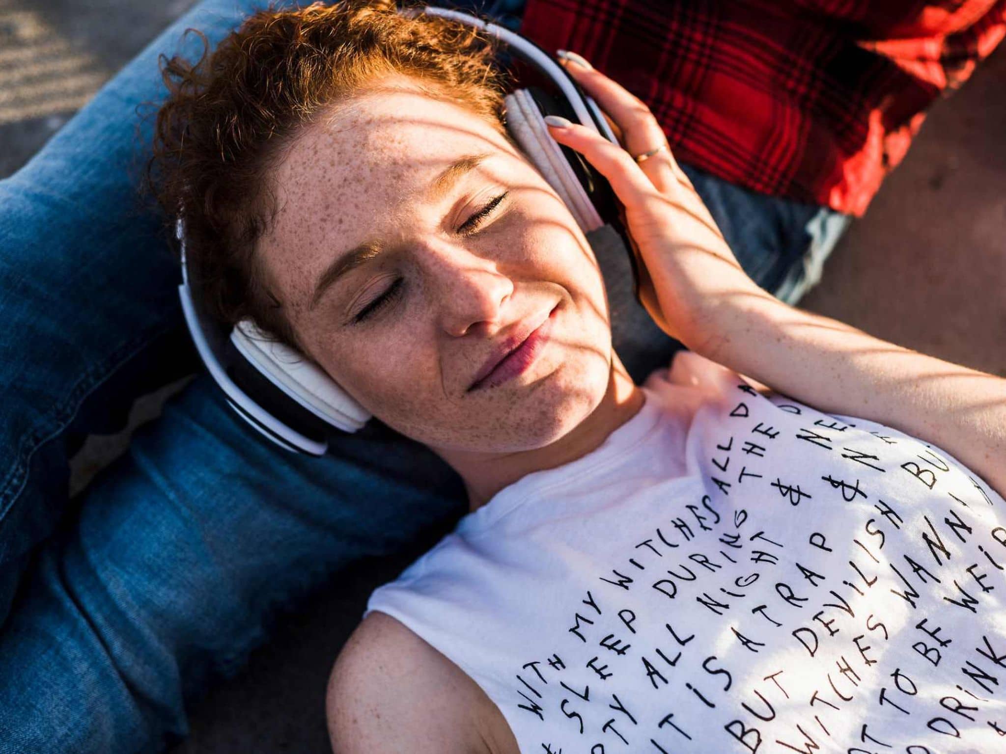 Bild: Frau mit roten Haaren und Kopfhörern liegt auf den Beinen ihres Freundes.