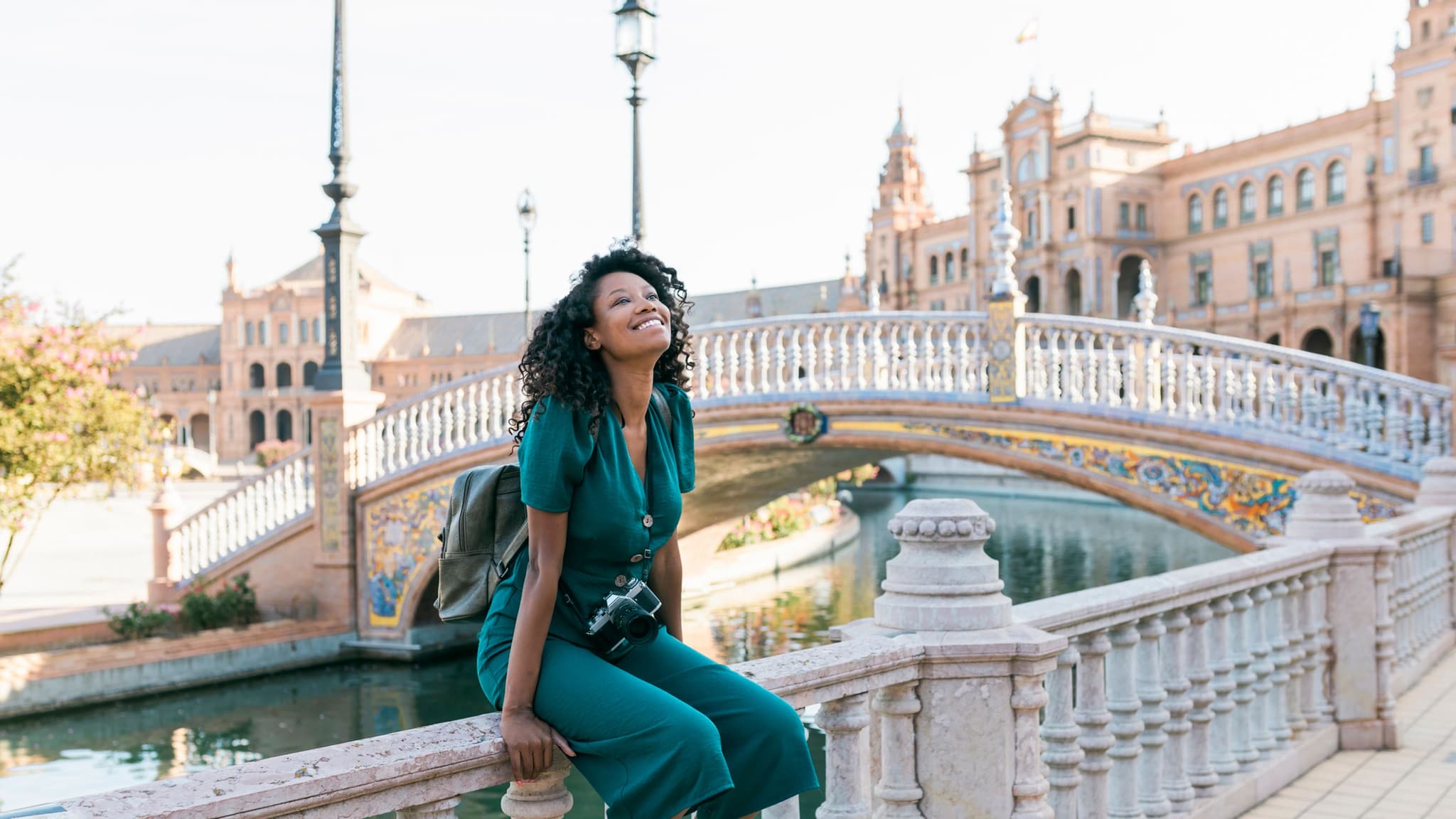 Langzeitaufenthalt Ausland: Junge Frau sitzt auf Geländer einer alten Brücke in Sevilla.