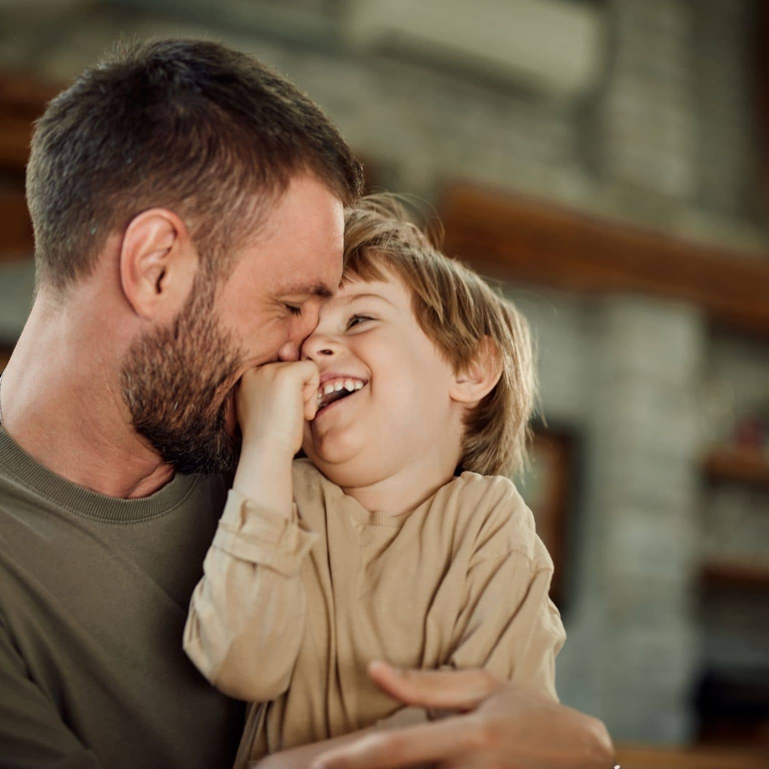 DAK AktivBonus Junior: Lachender Junge sitzt auf dem Schoß seines Vaters