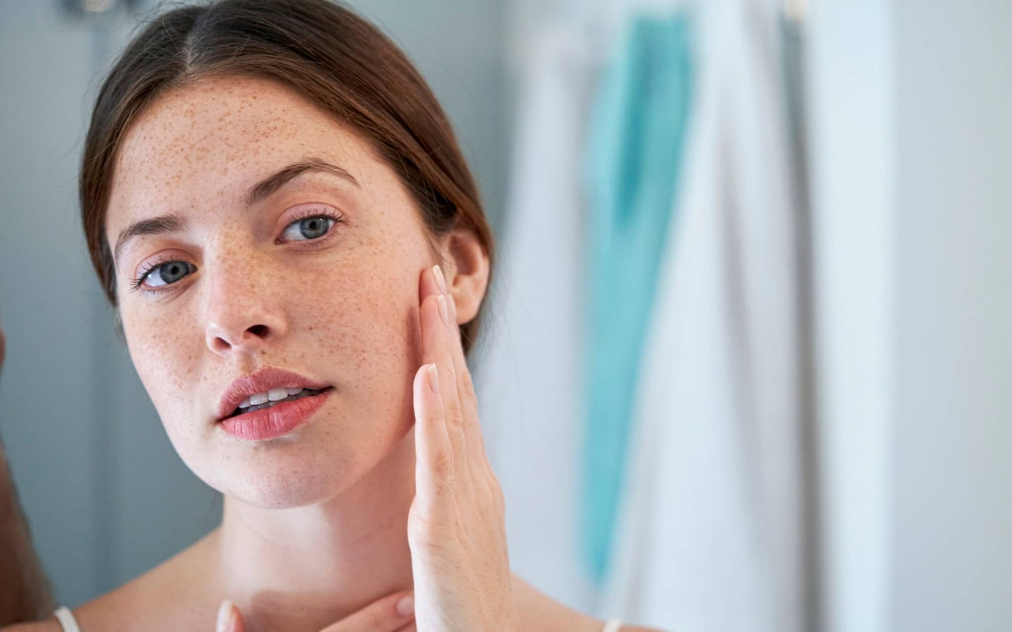 Junge Frau betrachtet ihr Spiegelbild und berührt ihr Gesicht mit der Hand.