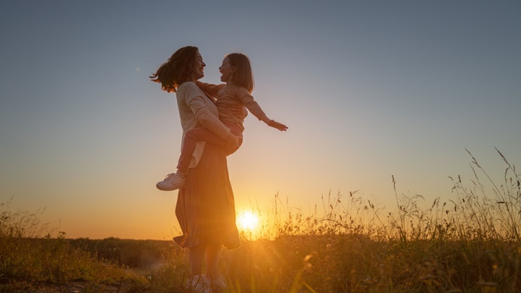 Mutter dreht Tochter im Kreis in der Natur während eines Sonnenuntergangs.