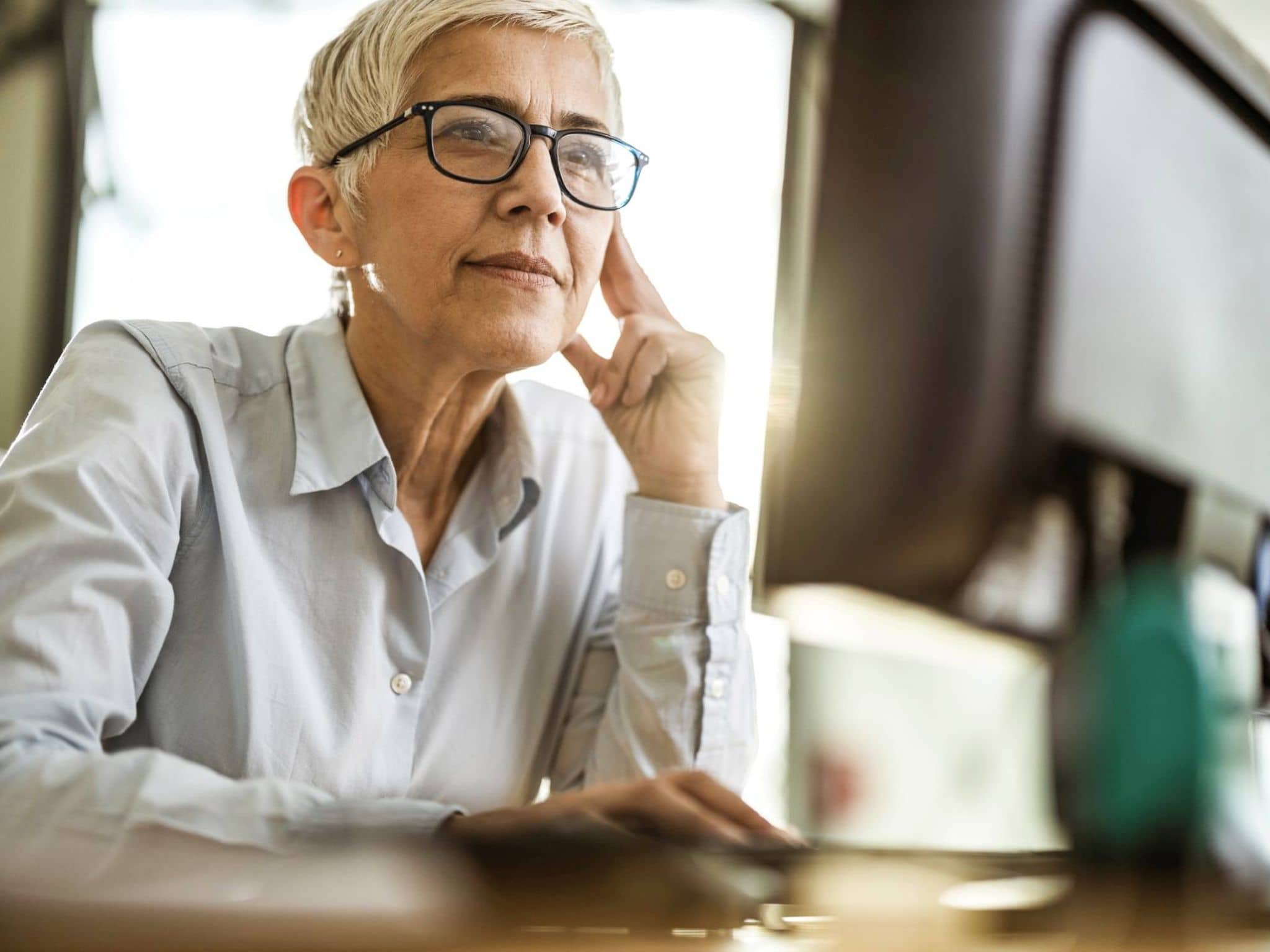 Bild: Frau mit Brille schaut etwas auf einem Computerbildschirm nach