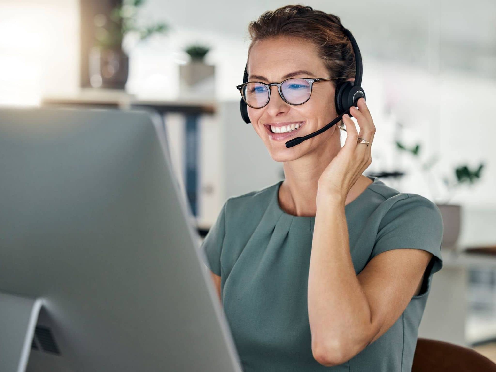 Bild: Lächelnde Frau mit Brille und Headset im Gespräch am Bildschirm