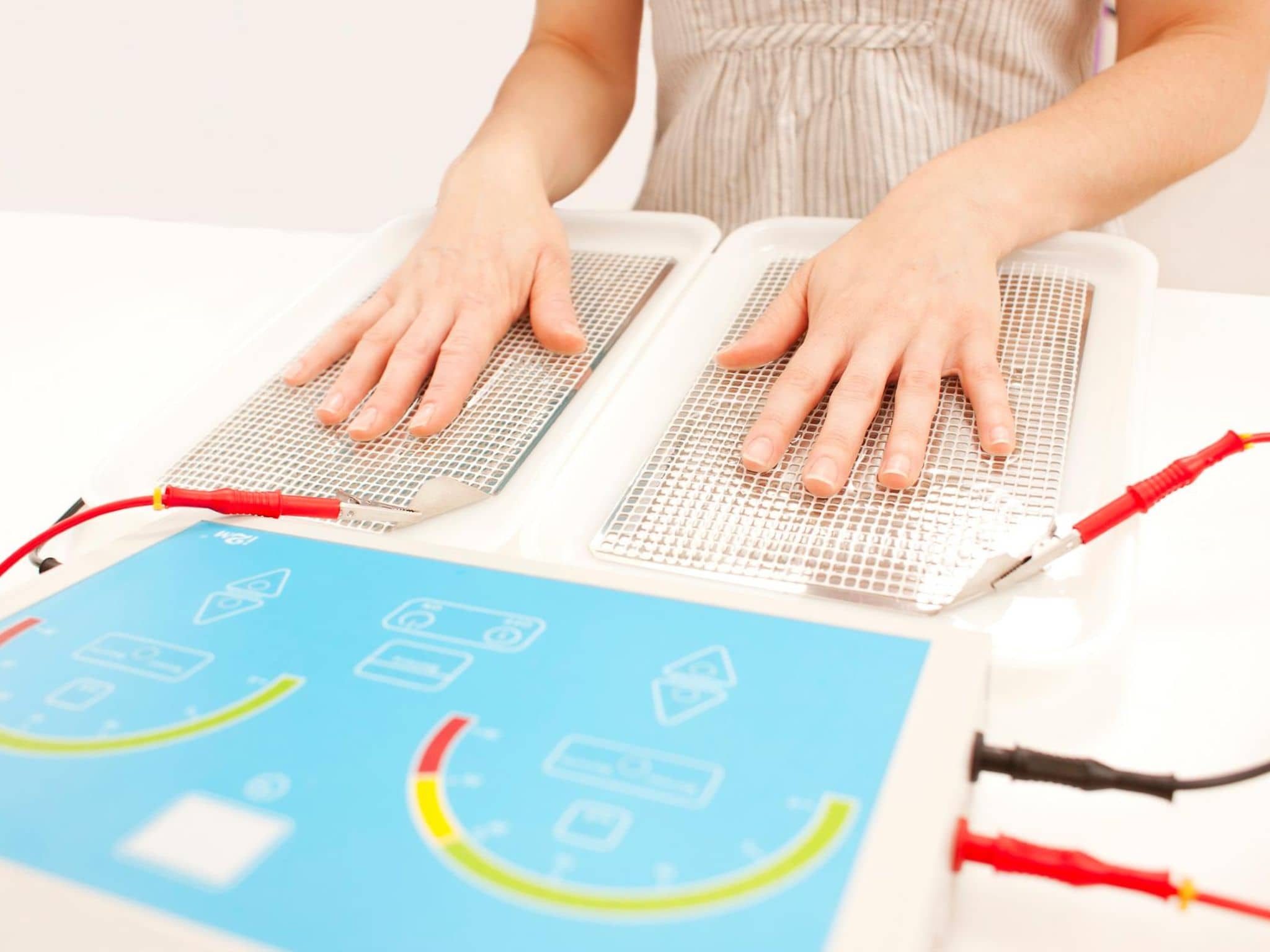 Bild: Frau nutzt ein Iontopheresegerät und hat dazu die Hände auf zwei Gittern platziert.