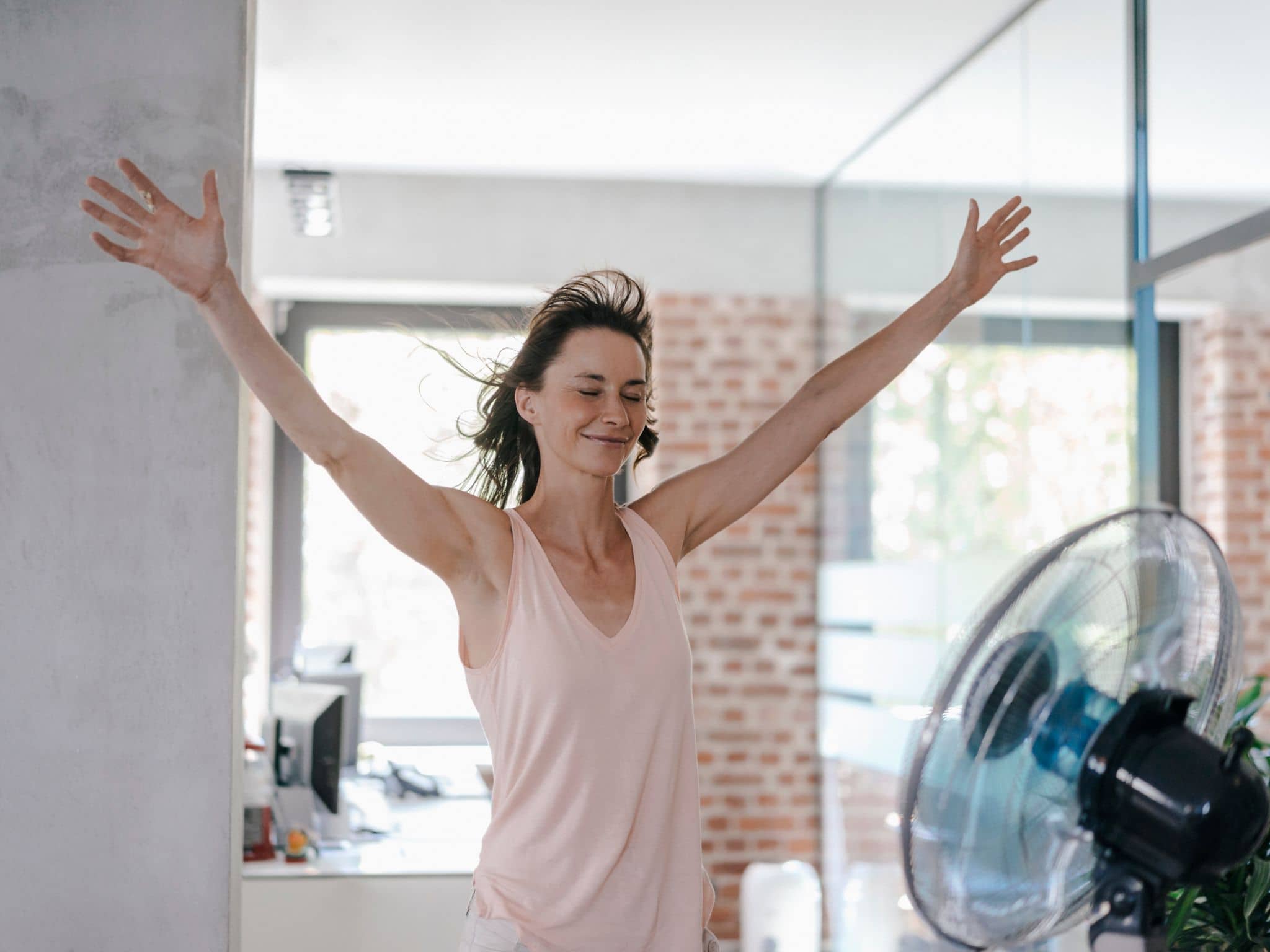 Frau bei Hitze im Büro vorm Ventilator