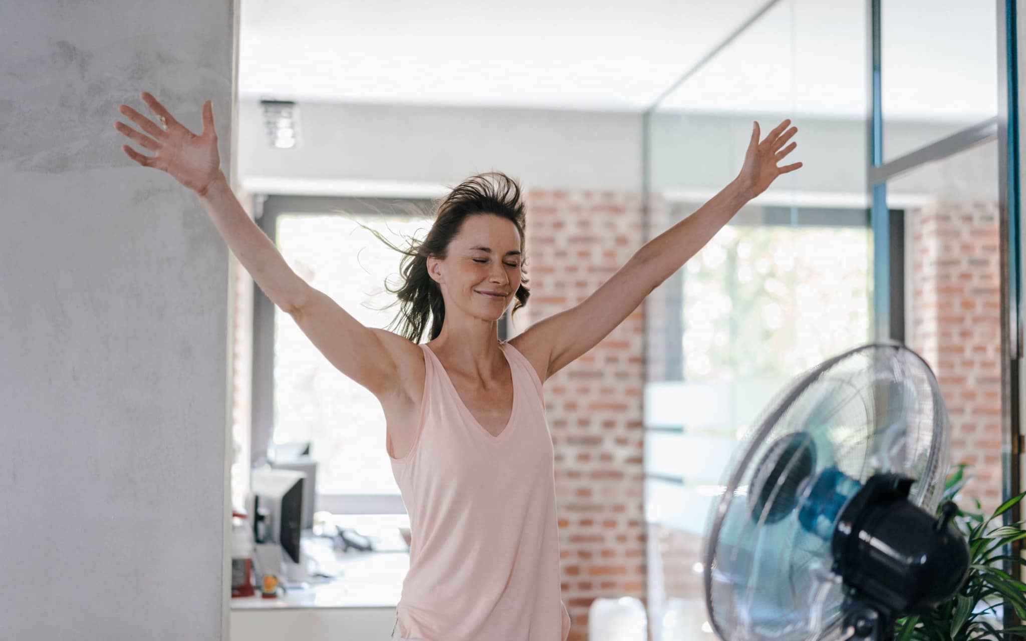 Frau bei Hitze im Büro vorm Ventilator